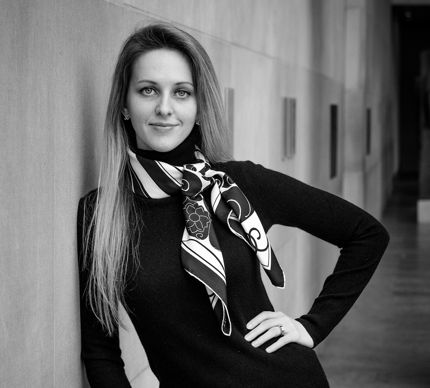 Shannon DeLong of DeLong Photography leaning against a wall in the metropolital museum of art gently smiling at the camera wearing a graphic scarf A black and white image of Shannon DeLong leaning on wall wearing a graphic scarf gently smiling at camera