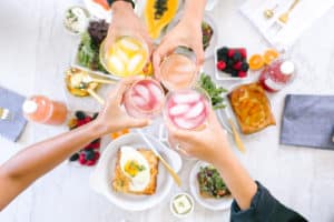 Wedding party cheersing iced colorful drinks above various foods on a marble table implying a cost of wedding planning