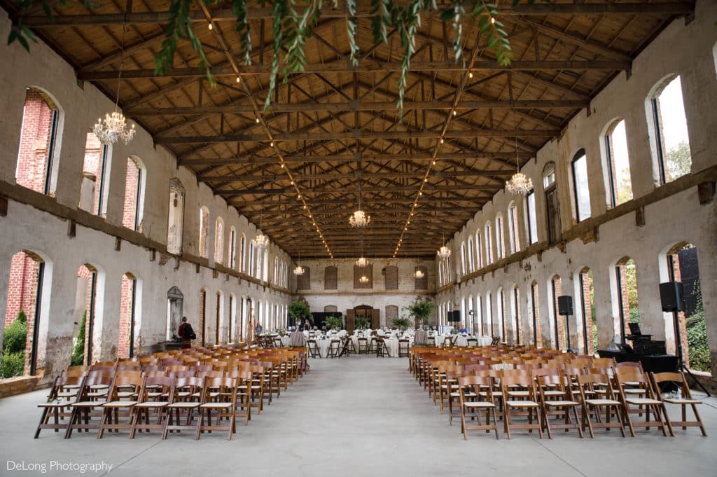 A wide shot of the interior of The Providence Cotton Mill completely set up for indoor ceremony at one end and and indoor reception at the other by Charlotte Wedding Photographers DeLong Photography
