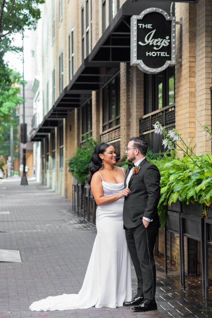 Interracial bride and groom smiling at one another on the street outside the Ivey's Hotel in Charlotte, NC by Charlotte wedding photographers DeLong Photography