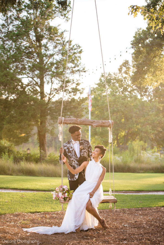 Bride sitting on swing smiling up at groom who is standing behind her at North Corner Haven by Charlotte Wedding Photographers DeLong Photography