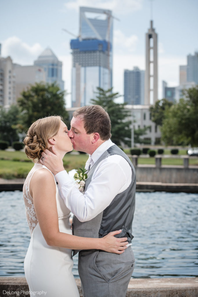 Bride and groom kissing in Marshall Park with Uptown city buildings in the background by Charlotte Wedding Photographers DeLong Photography