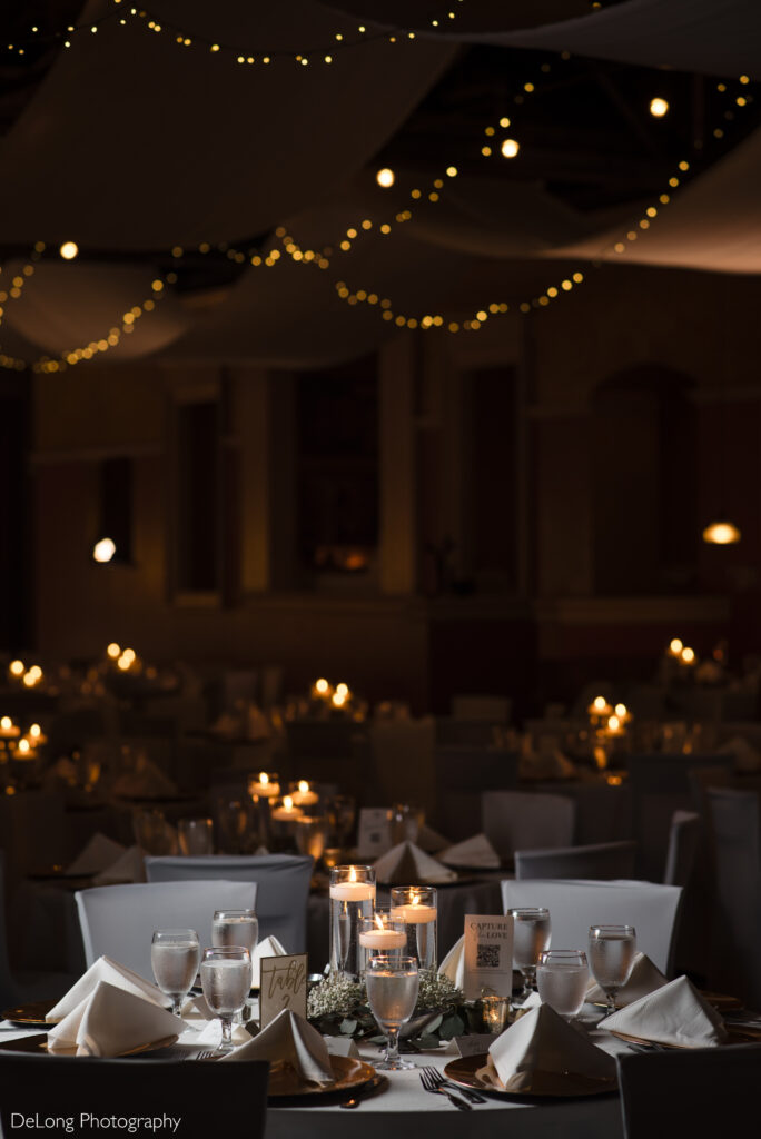 Elegant wedding reception setup at The Big Chill, a popular Charlotte wedding venue, featuring romantic candlelit centerpieces, crisp white linens, and soft string lights overhead—perfect for couples seeking an intimate, upscale wedding atmosphere in North Carolina. Photograph by DeLong Photography.