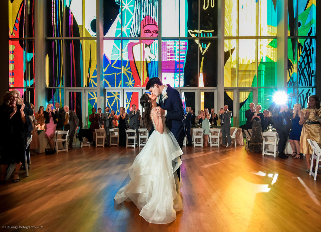 Bride and groom kissing during first dance in front of the glass wall at the Mint Museum Uptown by Charlotte wedding photographers DeLong Photography