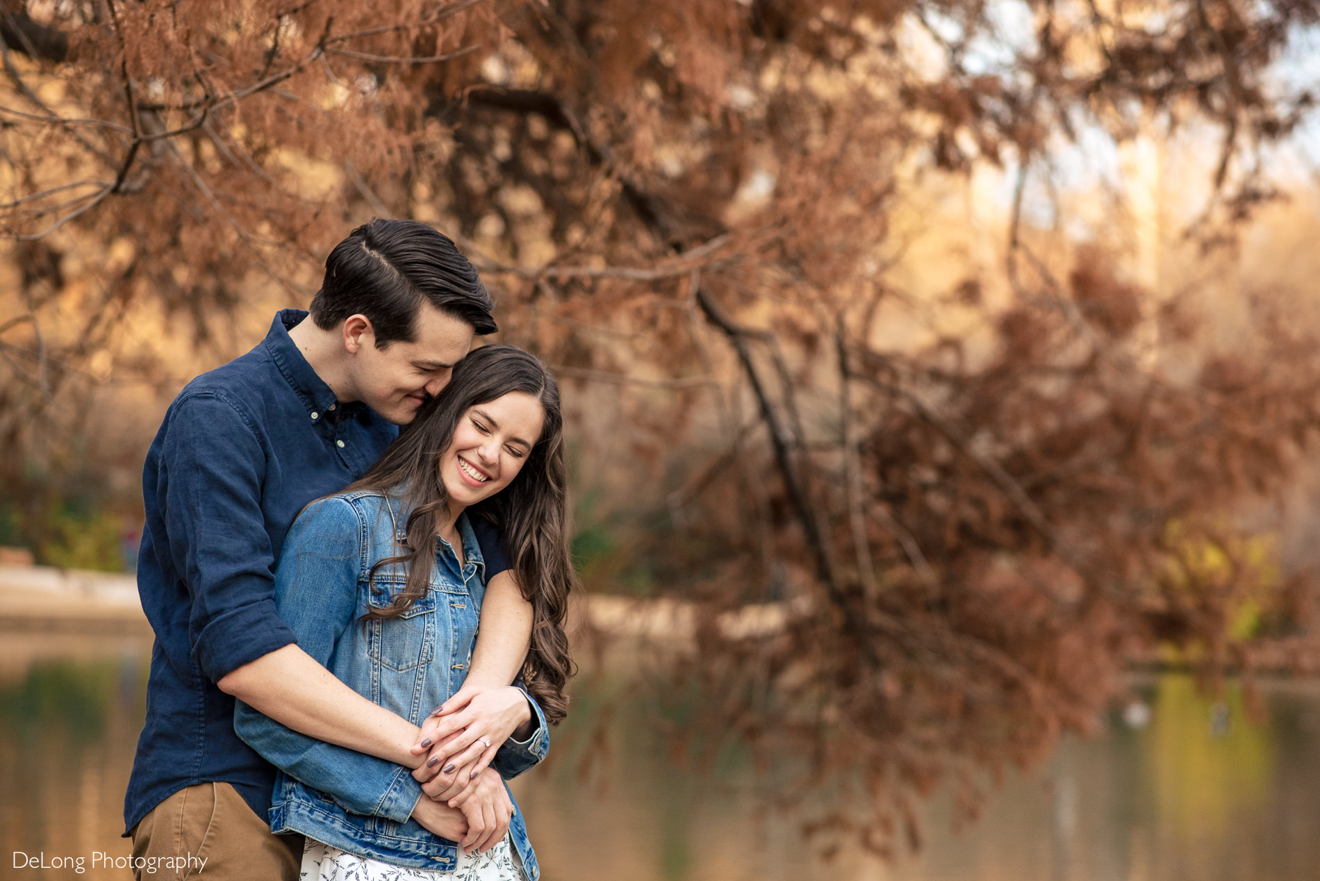 Engaged couple hugging and giggling outside near the pond at Freedom Park by Charlotte wedding photographers DeLong Photography