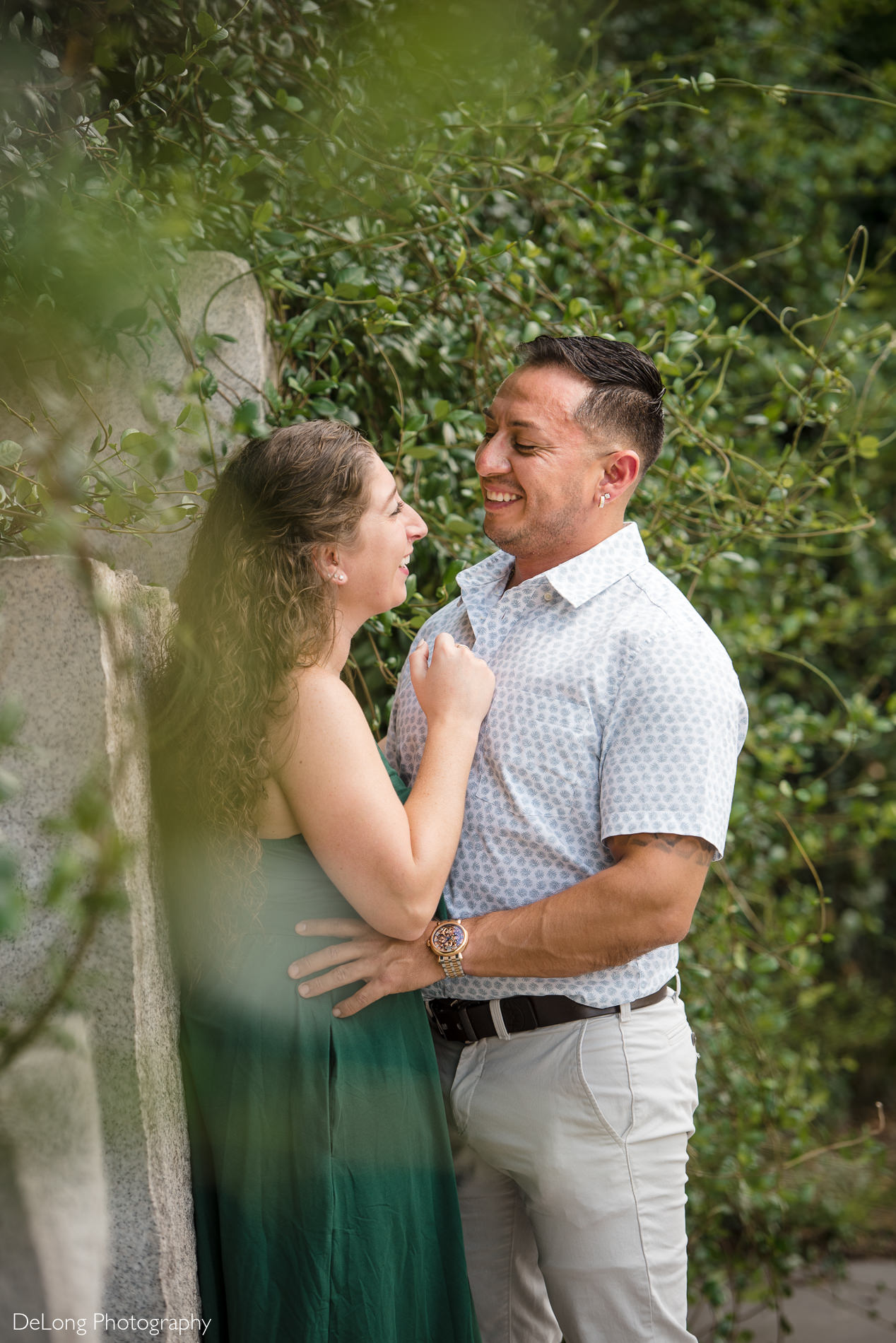 Man smiling lovingly at woman surrounded by greenery during a Romare Bearden Park engagement session by Charlotte wedding photographers DeLong Photography
