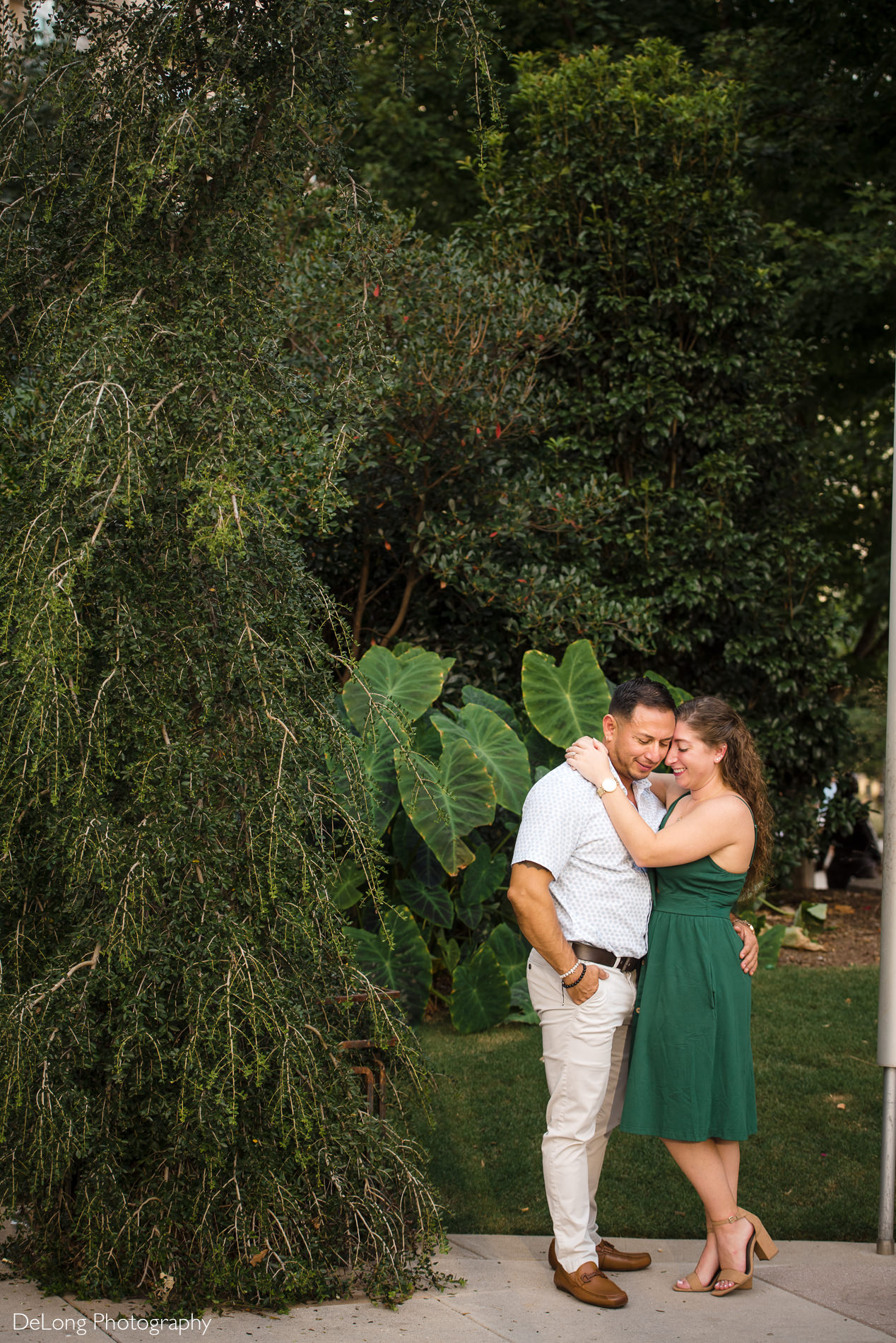Couple snuggling with arms around each other surrounded by greenery during a Romare Bearden Park engagement session by Charlotte wedding photographers DeLong Photography