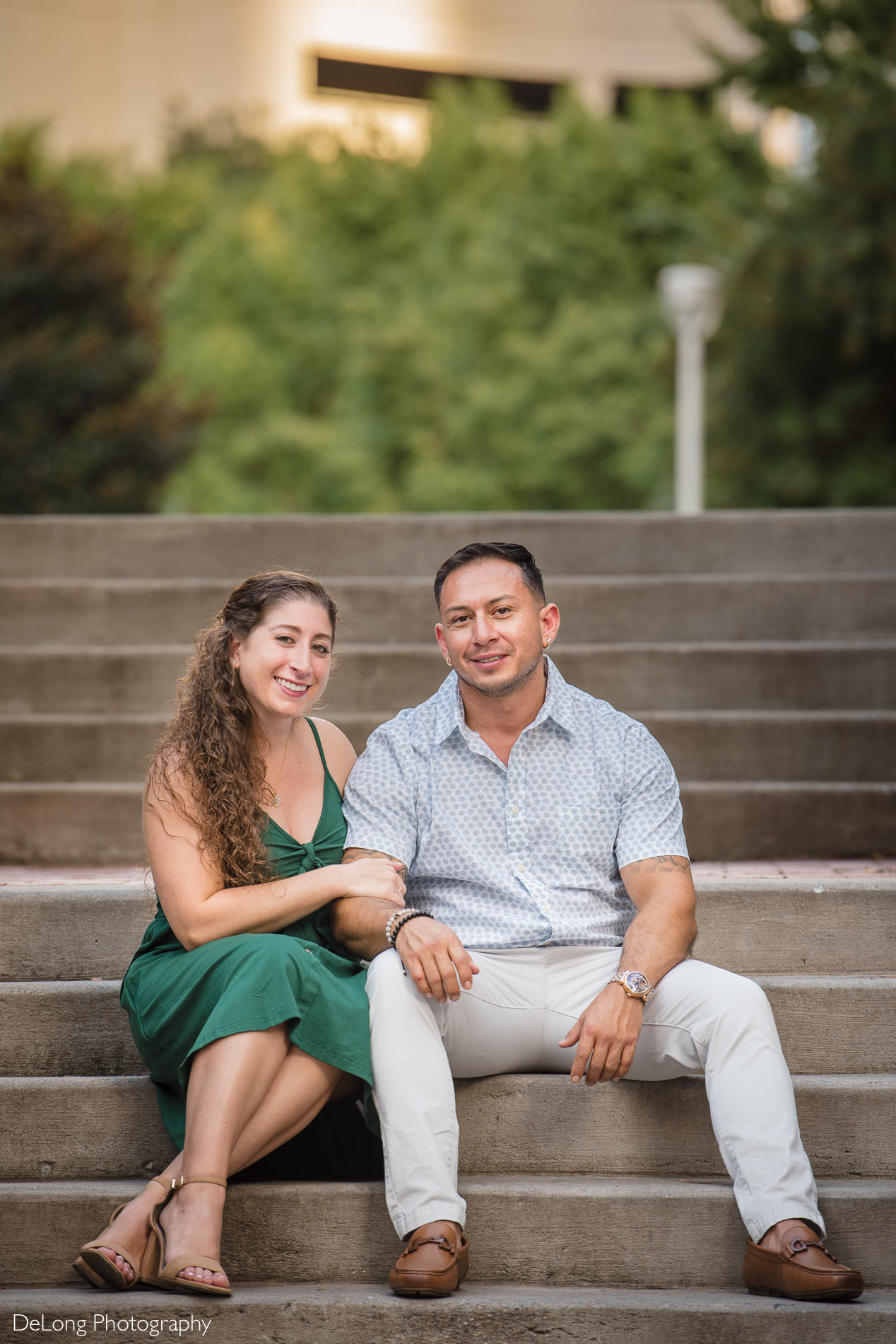 Couple sitting on stairs smiling during a Romare Bearden Park engagement session by Charlotte wedding photographers DeLong Photography