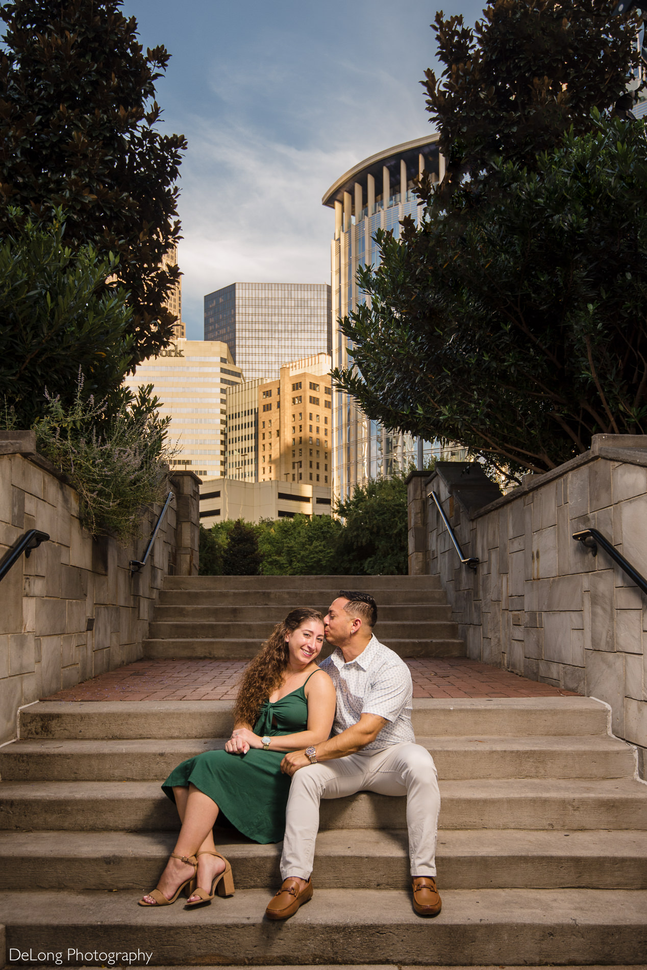 Man kissing woman's head snuggled up on stairs during a Romare Bearden Park engagement session by Charlotte wedding photographers DeLong Photography