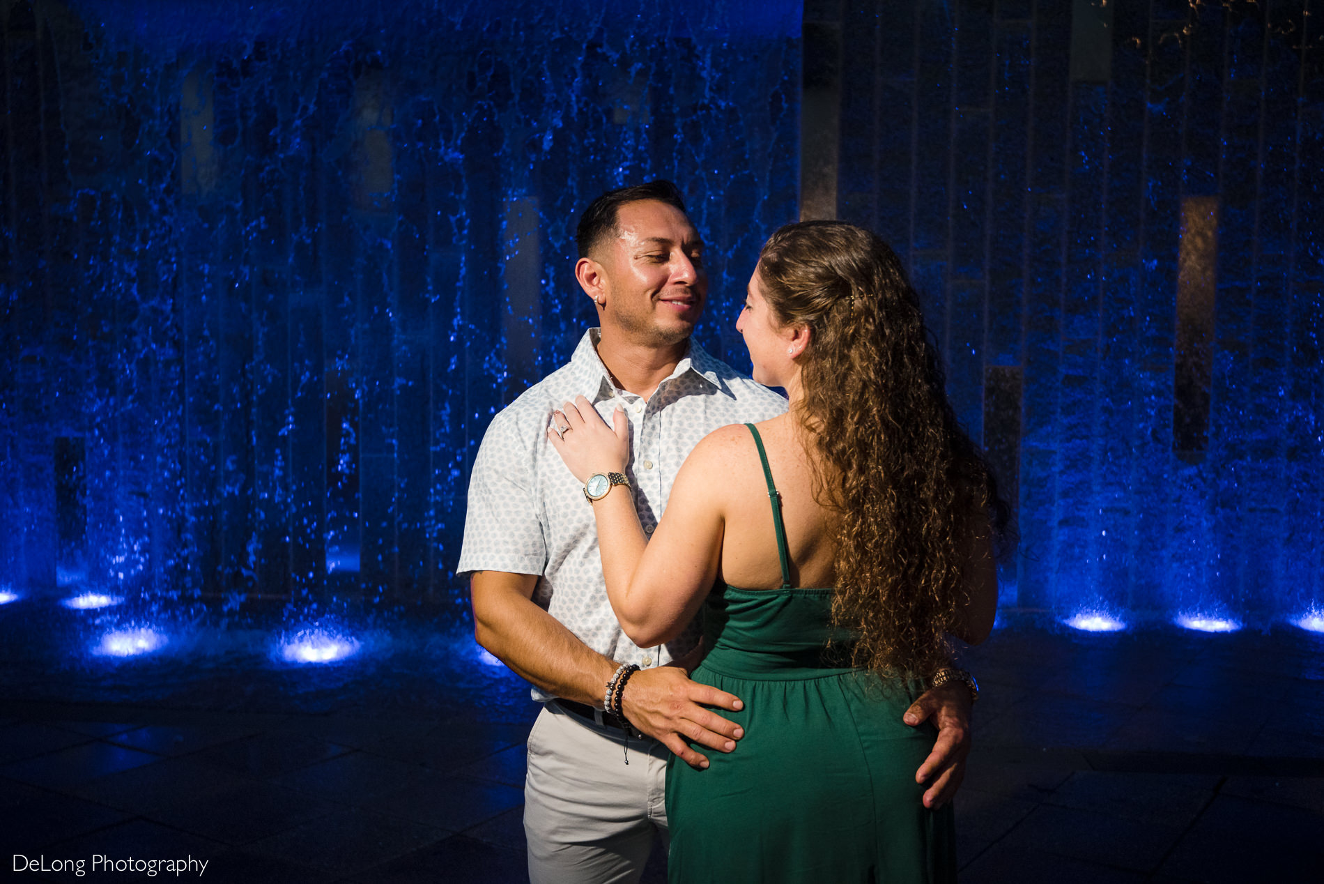 Man smiling at woman posed in front of water feature during a Romare Bearden Park engagement session by Charlotte wedding photographers DeLong Photography