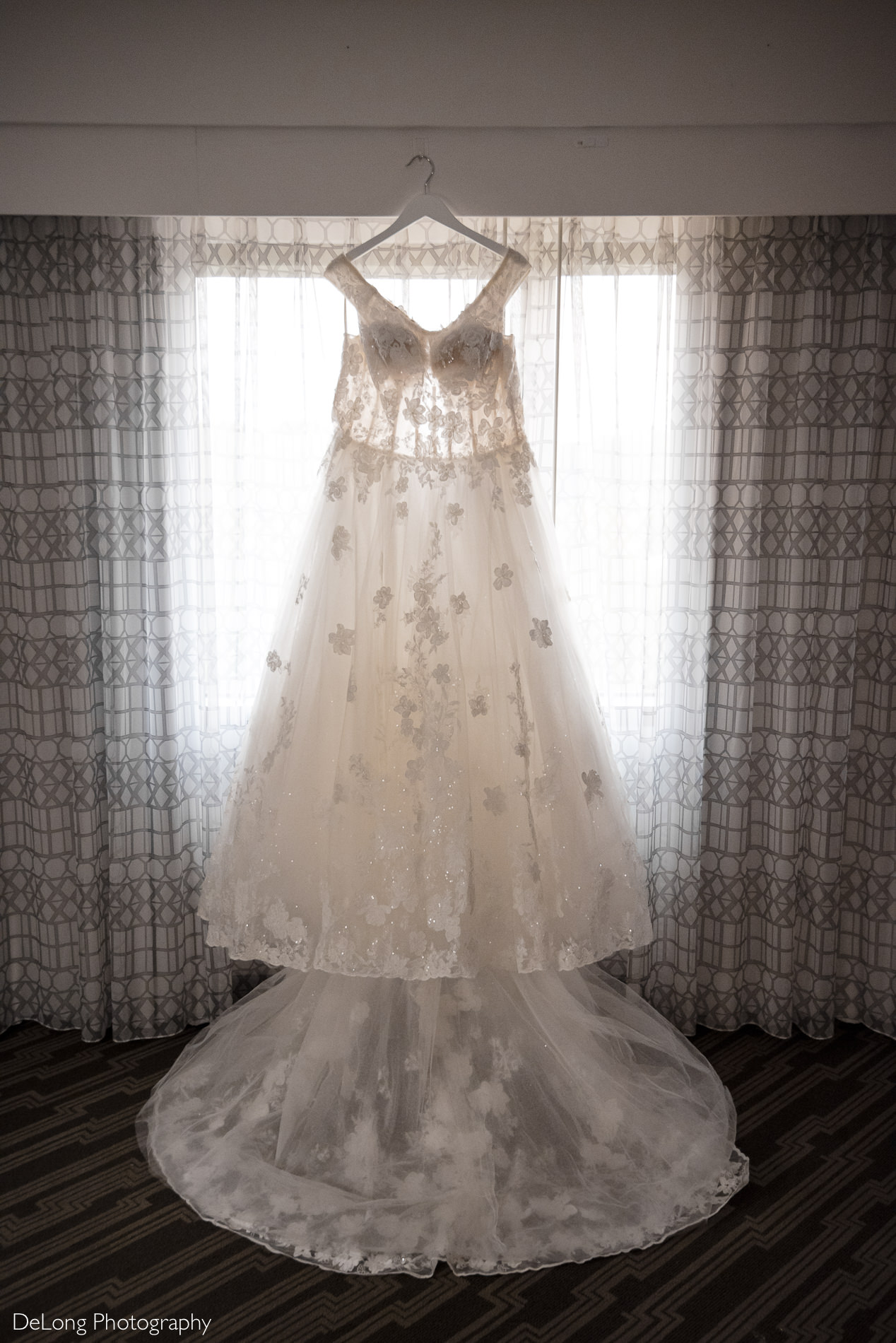 Bride's wedding dress hanging in Embassy Suites by Hilton Charlotte window by Charlotte wedding photographers DeLong Photography