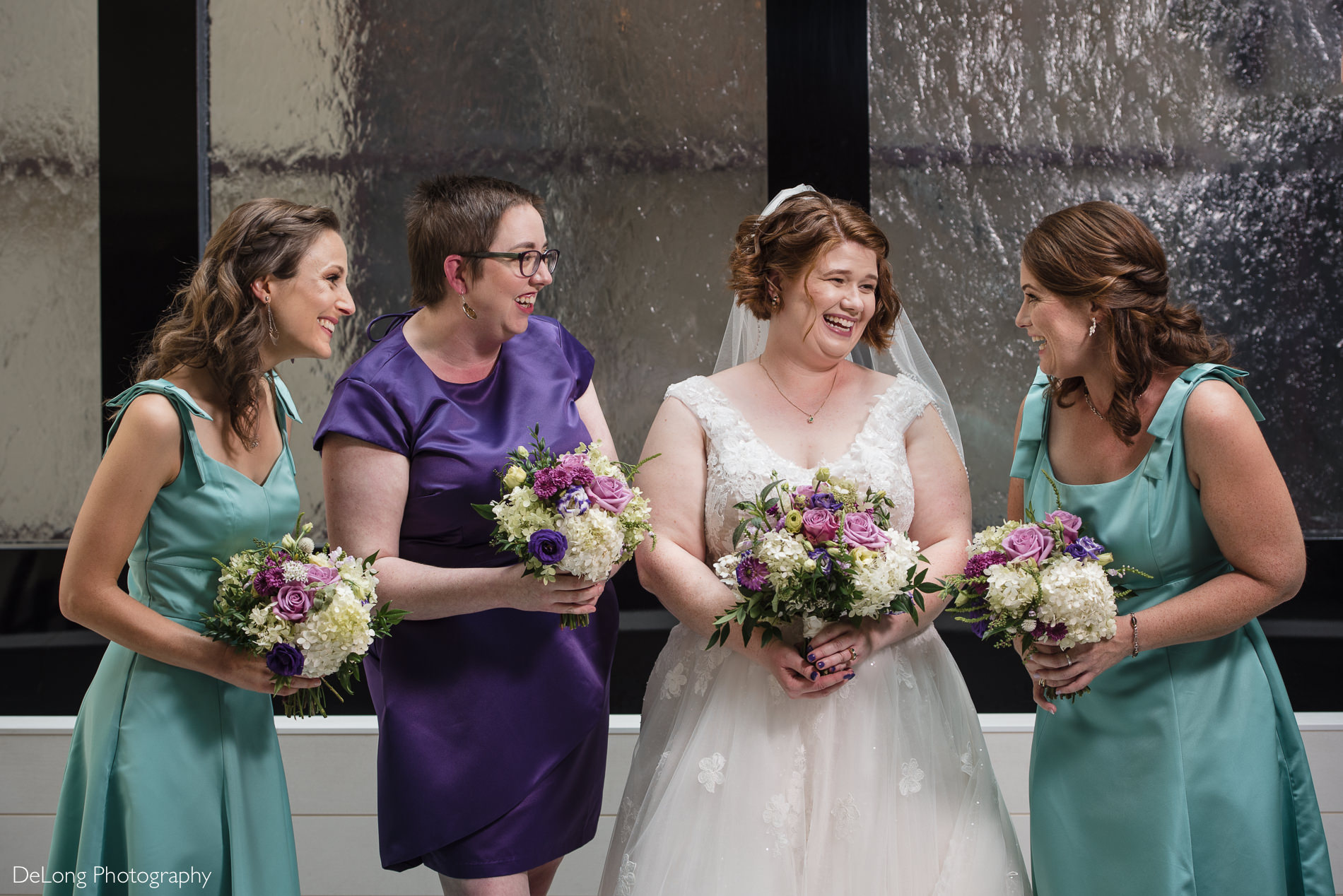 Bride and bridesmaids happy photo in atrium of Embassy Suites by Hilton Charlotte by Charlotte wedding photographers DeLong Photography