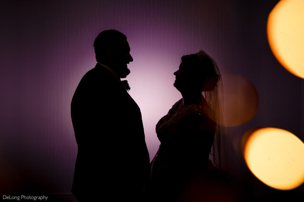 Silhouette of bride and groom smiling at each other in front of a purple wall at the Embassy Suites by Hilton Charlotte by Charlotte wedding photographers DeLong Photography