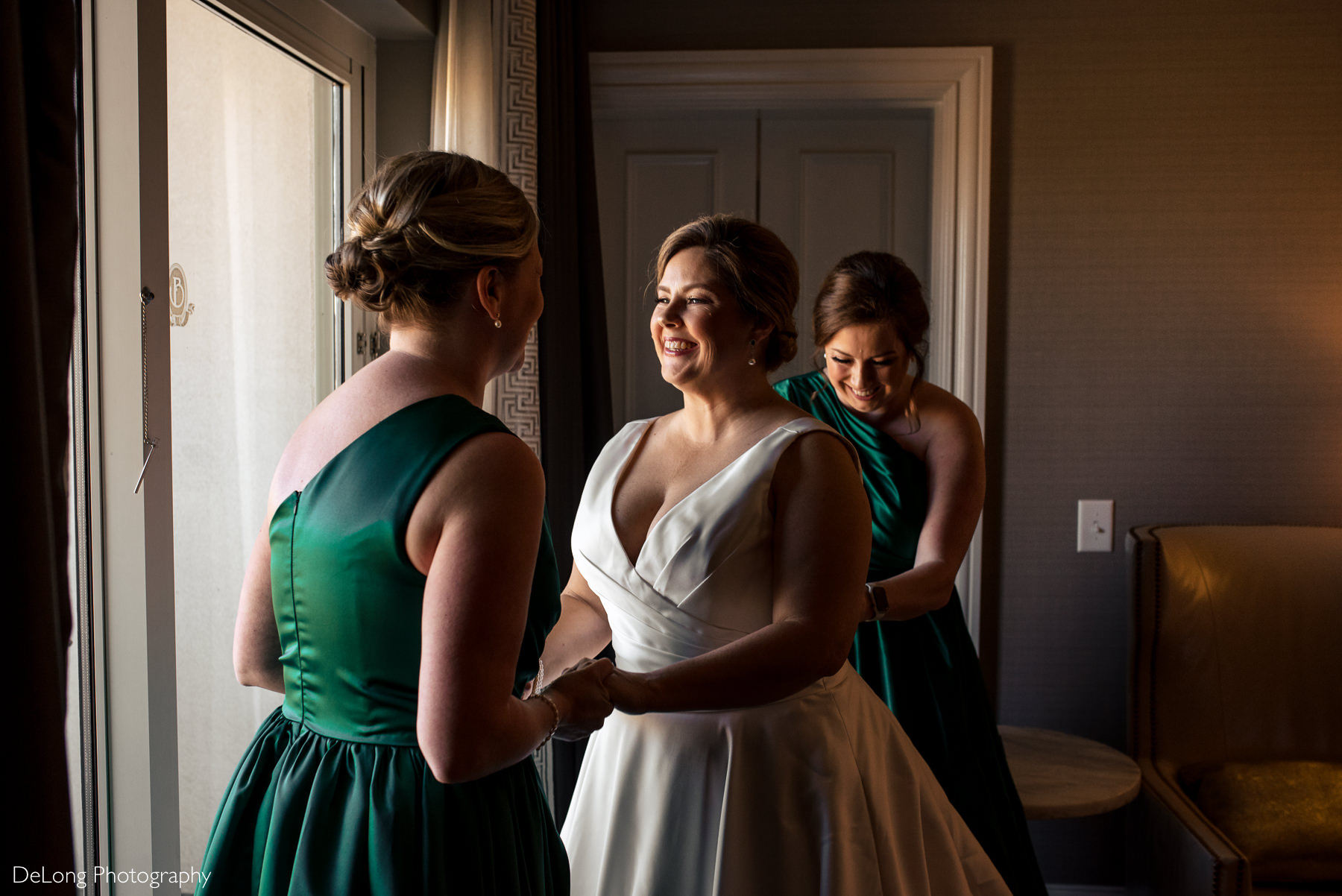 Bride laughing with friend as matron of honor buttons her dress by Charlotte Wedding Photographers DeLong Photography