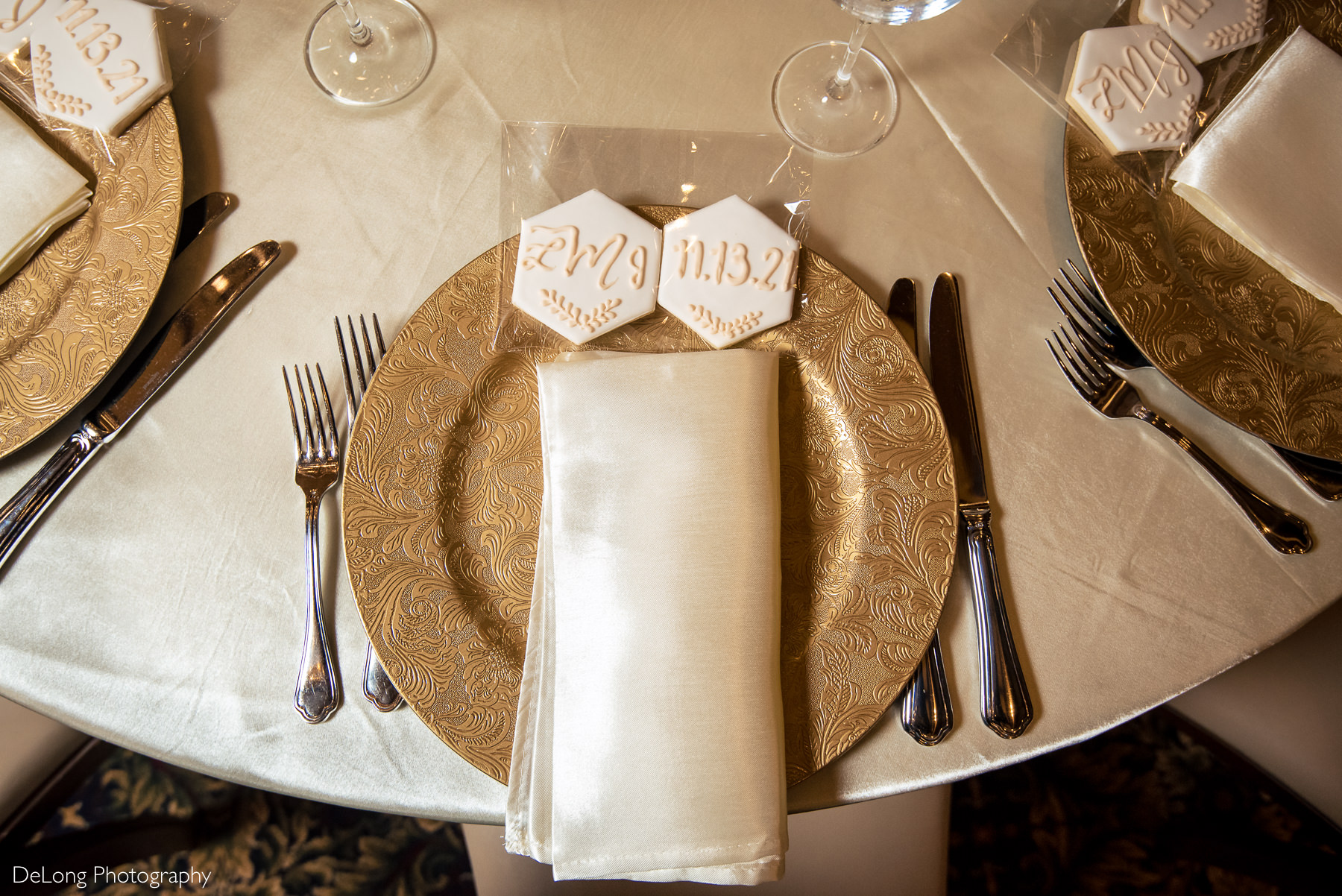 White hexagonal cookies with the bride and groom's initials and wedding date on them placed on gold charger at wedding reception at The Club at Longview by Charlotte Wedding Photographers DeLong Photography