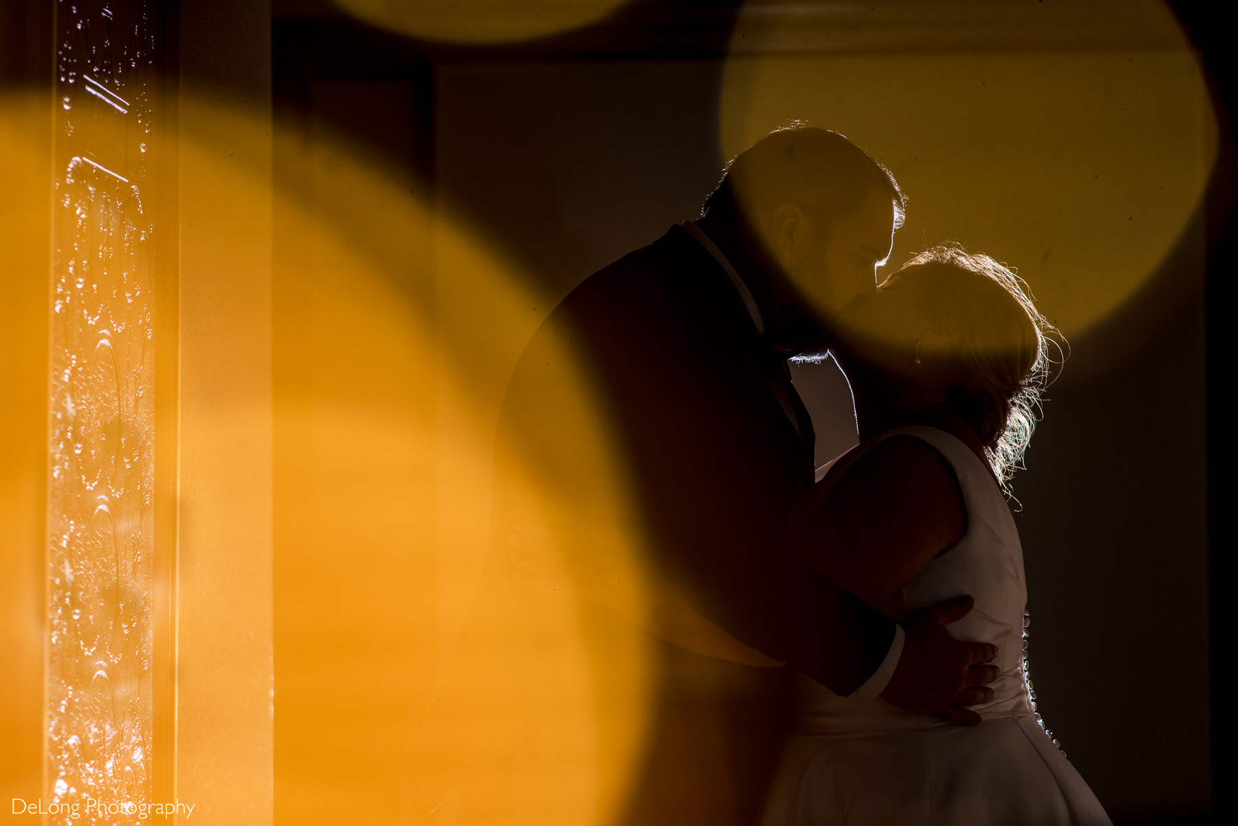 Rim lit indoor bride and groom portrait kissing with bokeh lights Bride and groom night portrait in front of fountain at The Club at Longview wedding by Charlotte Wedding Photographers DeLong Photography
