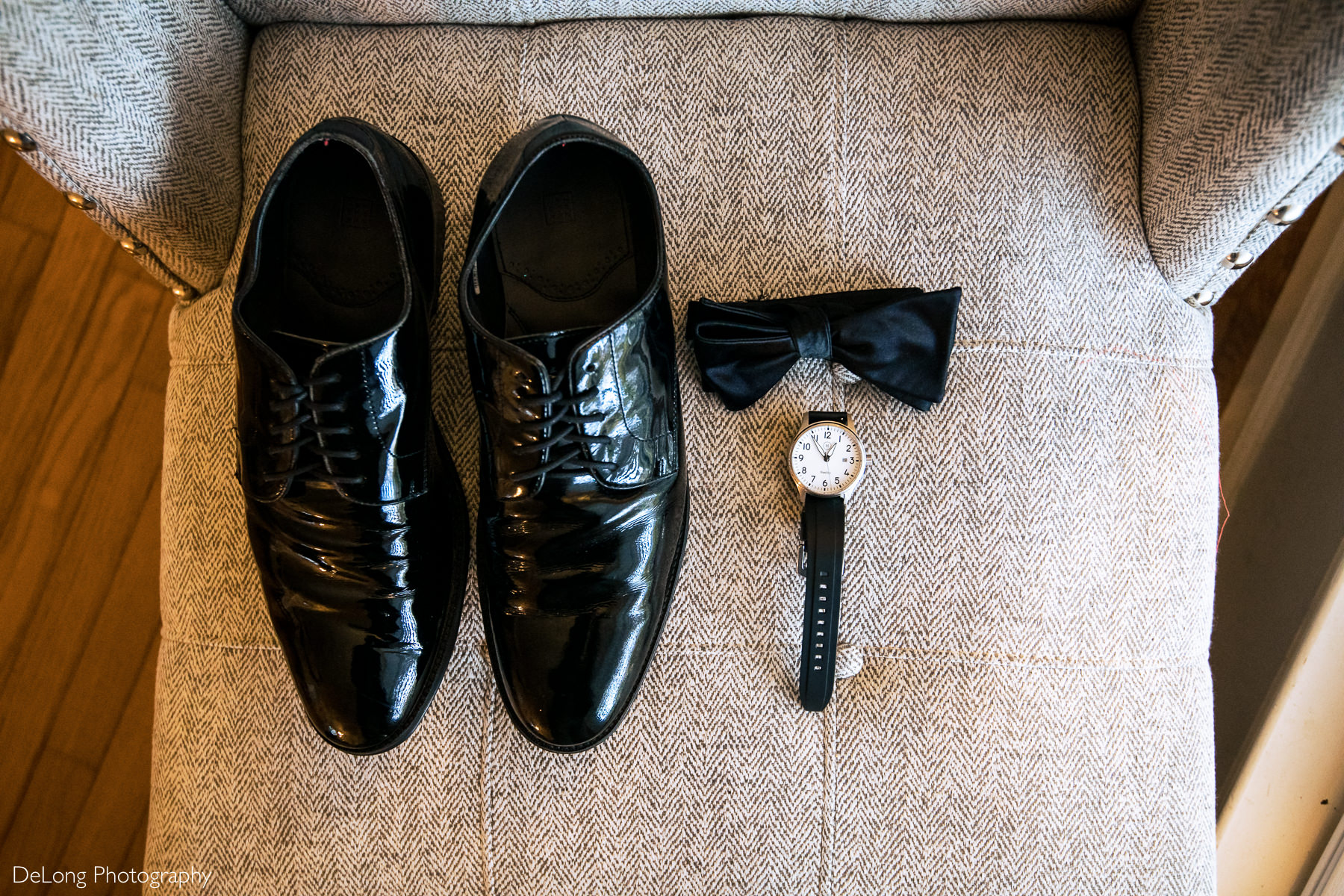 Groom's polished black shoes, black tie, and black watch on a grey side chair displaying his wedding details by Charlotte wedding photographers DeLong Photography