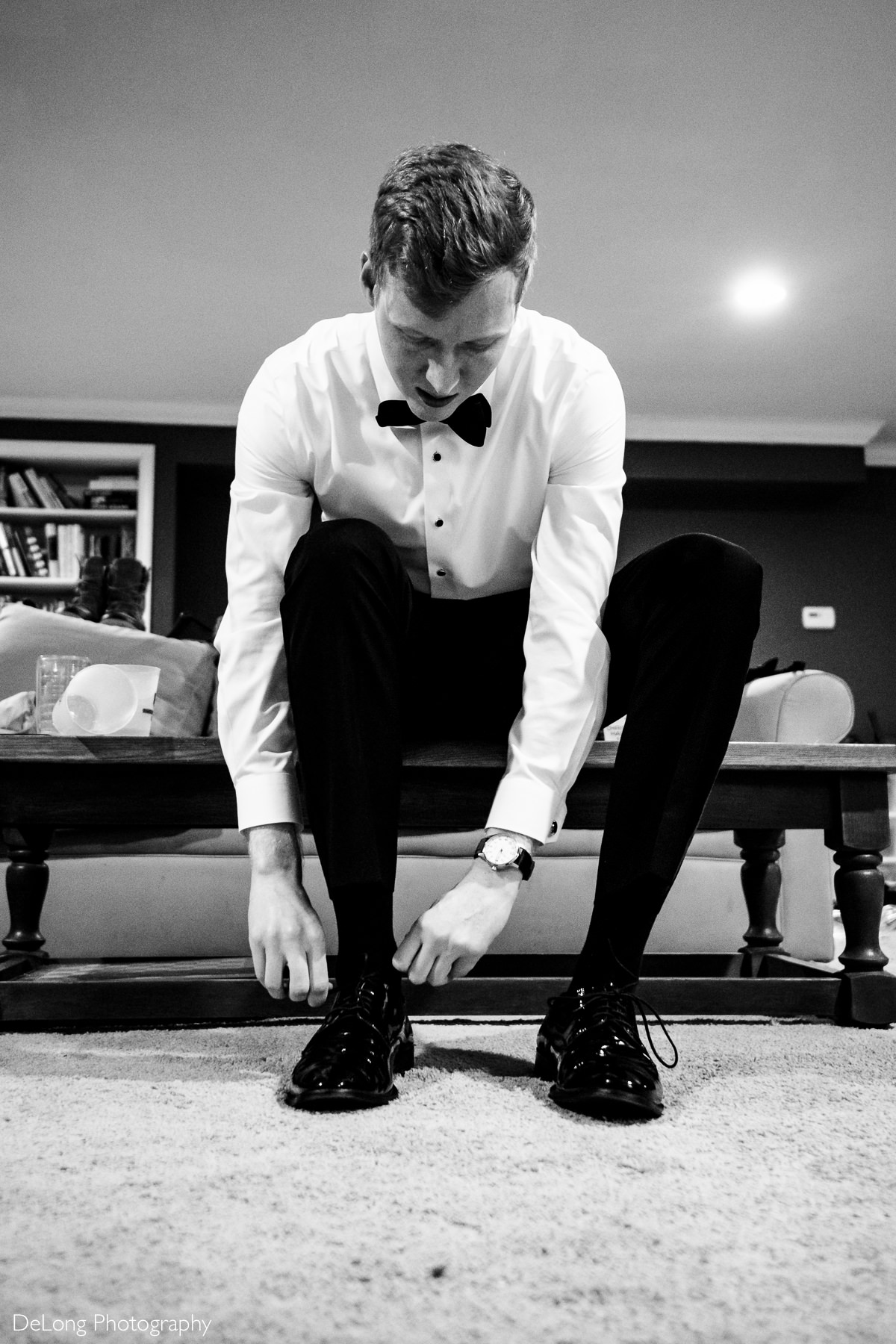 Black and white image of the groom tying his shoes during the getting-ready portion of the wedding day by by Charlotte wedding photographers DeLong Photography