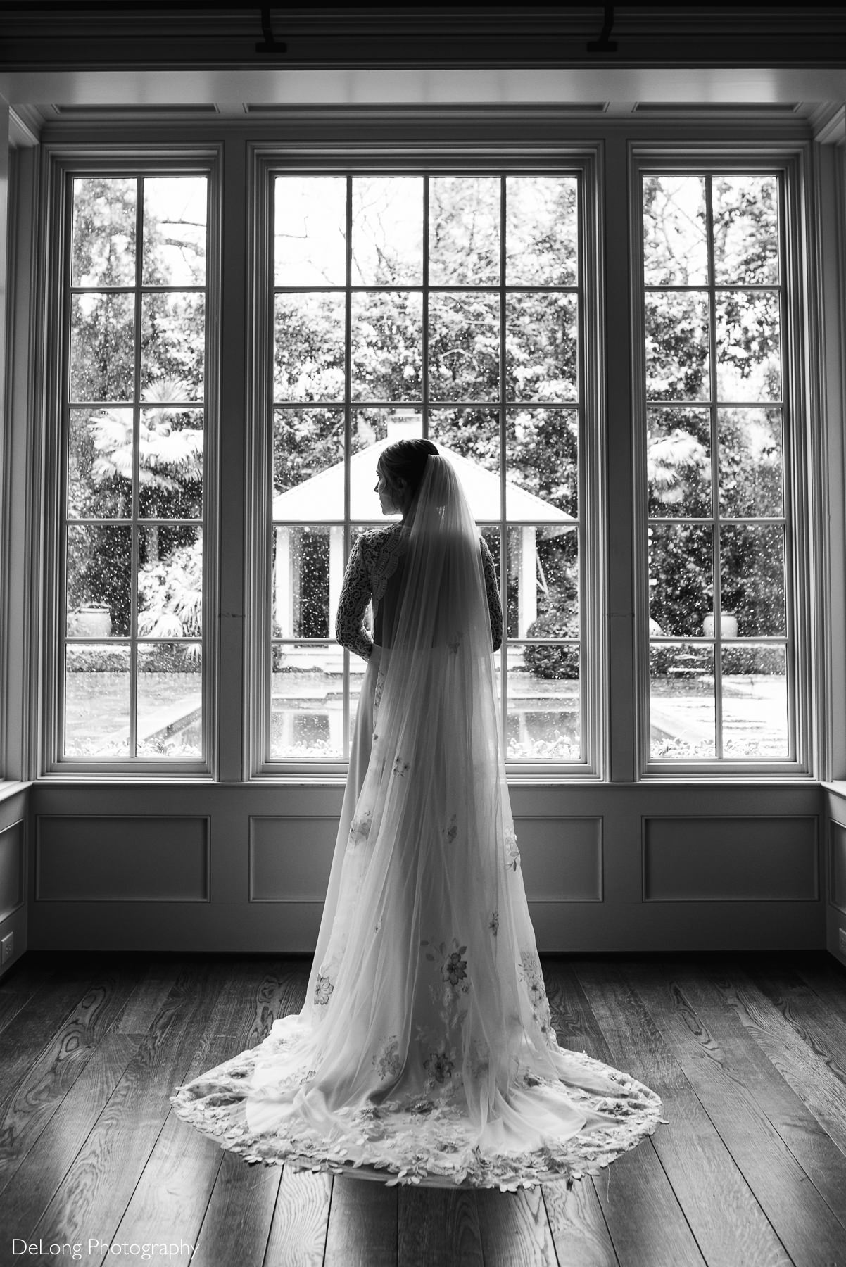 Black and white silhouette portrait of a bride in a Lulus wedding dress standing in front of large windows showing the snow falling outside by Charlotte wedding photographers DeLong Photography