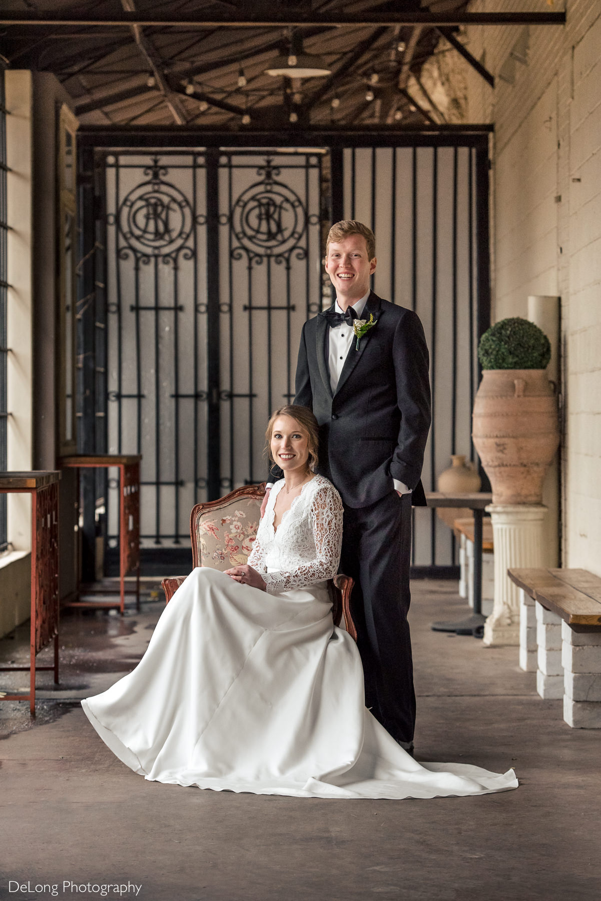 Bride seated while the groom stands next to her for a formal portrait at the Westside Warehouse in Atlanta by Charlotte wedding photographers DeLong Photography