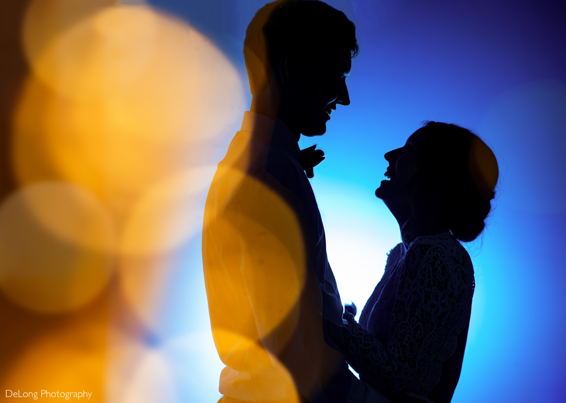 Silhouette of bride and groom laughing and smiling on a blue background with golden bokeh balls in the foreground by Charlotte wedding photographers DeLong Photography