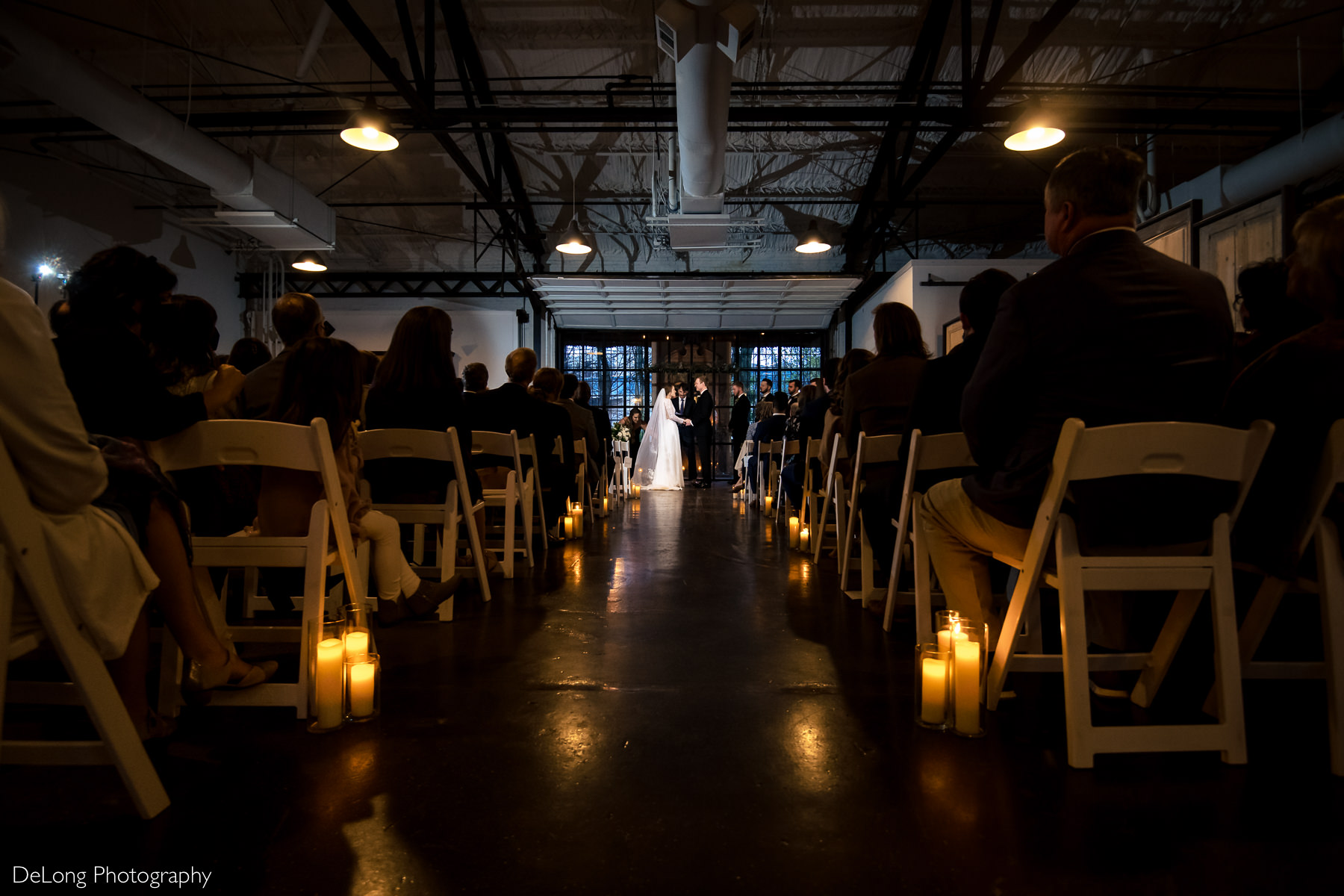 Wide and low angle photograph of a wedding ceremony aisle lined with candles indoors at the Westside Warehouse by Charlotte wedding photographers DeLong Photography