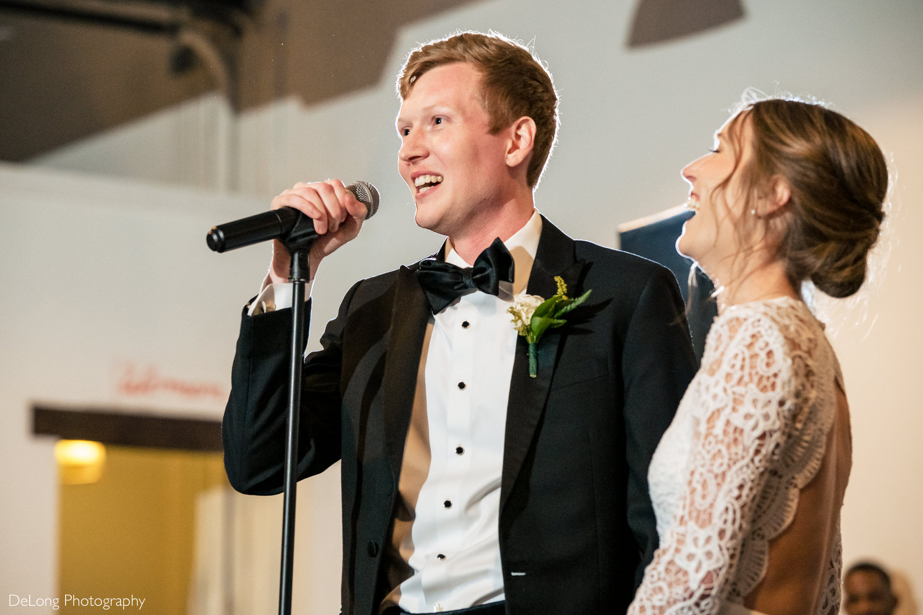 Close up of a groom smiling during a welcome speech and his bride is laughing beside him at the Westside warehouse in Atlanta by Charlotte wedding photographers DeLong Photography