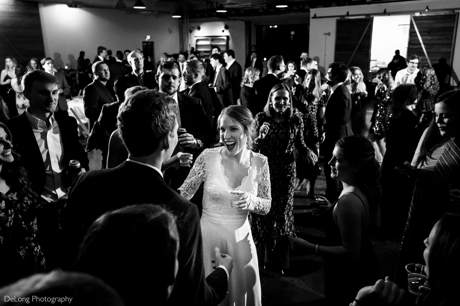 Black and white image from a high angle showing a packed dance floor with the bride smiling at her groom in the middle of the crowd at the Westside warehouse in Atlanta by Charlotte wedding photographers DeLong Photography