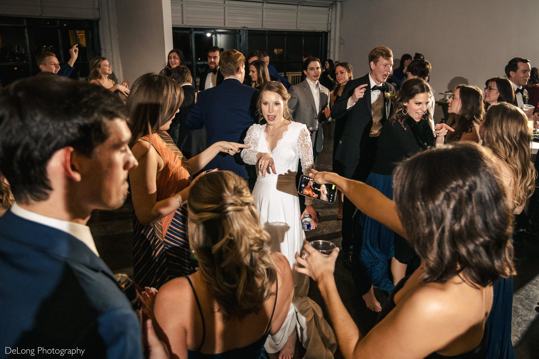 Bride and friends in a circle on the dancing floor pointing at one another singing lyrics to a song at the Westside warehouse in Atlanta by Charlotte wedding photographers DeLong Photography