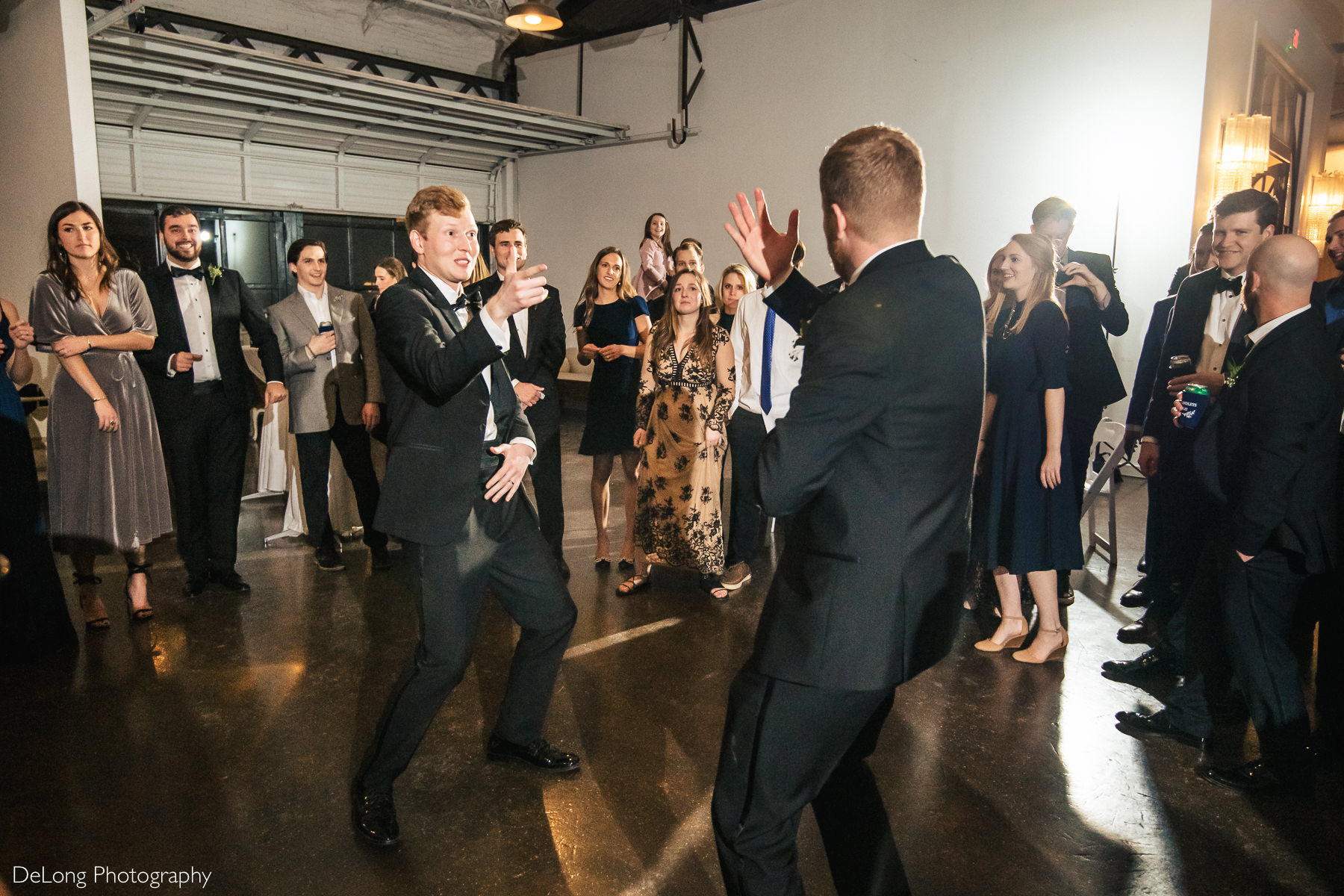 Groom and his brother in the middle of the dance floor having a dance battle while reception guests are circled around them at the Westside warehouse in Atlanta by Charlotte wedding photographers DeLong Photography