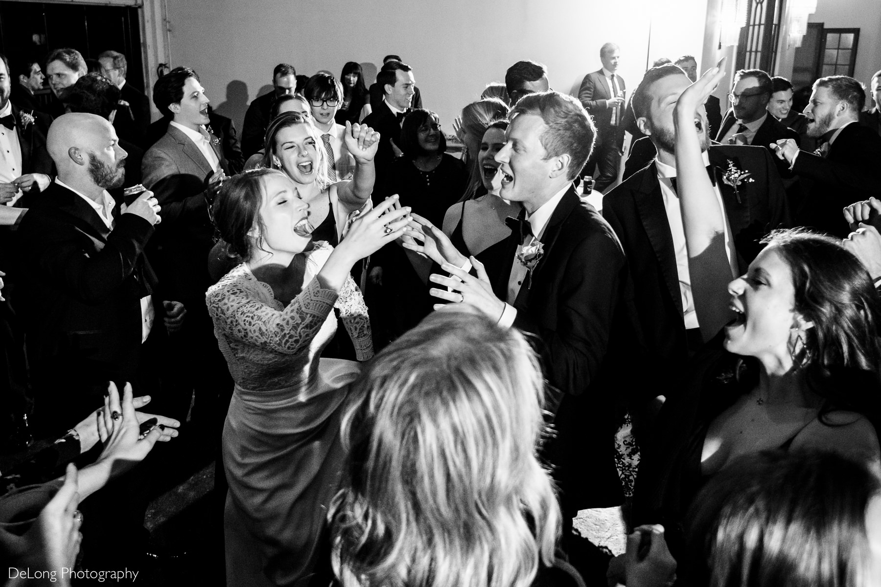 Black and white high angle image of a packed dance floor with the bride and groom in the middle belting out the lyrics to a song with their hands in the air having fun at the Westside warehouse in Atlanta by Charlotte wedding photographers DeLong Photography