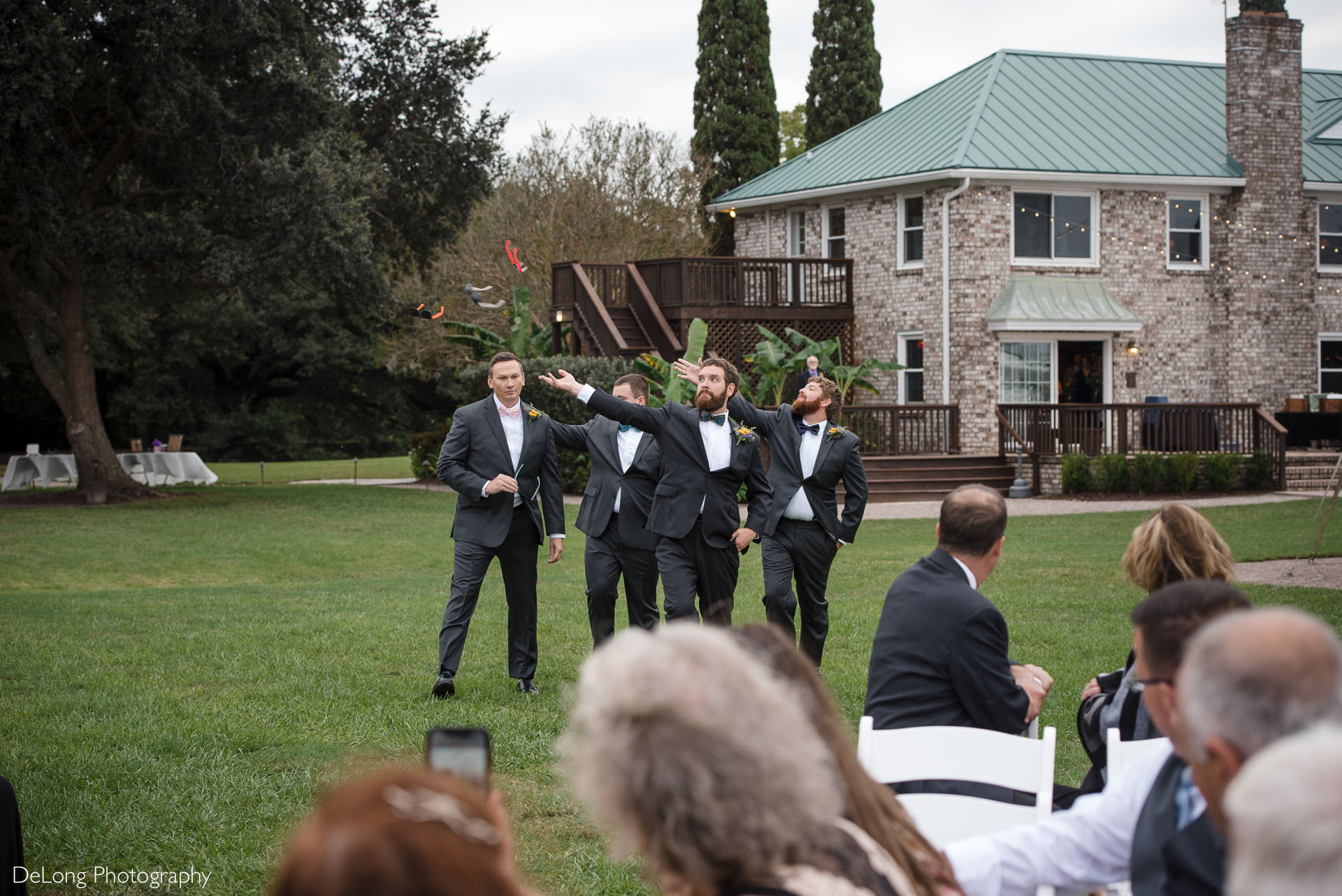 Groom and groomsmen doing a funny ceremony entrance by walking out throwing their sunglasses at the Island House in Charleston, SC by Charlotte Wedding Photographers DeLong Photography