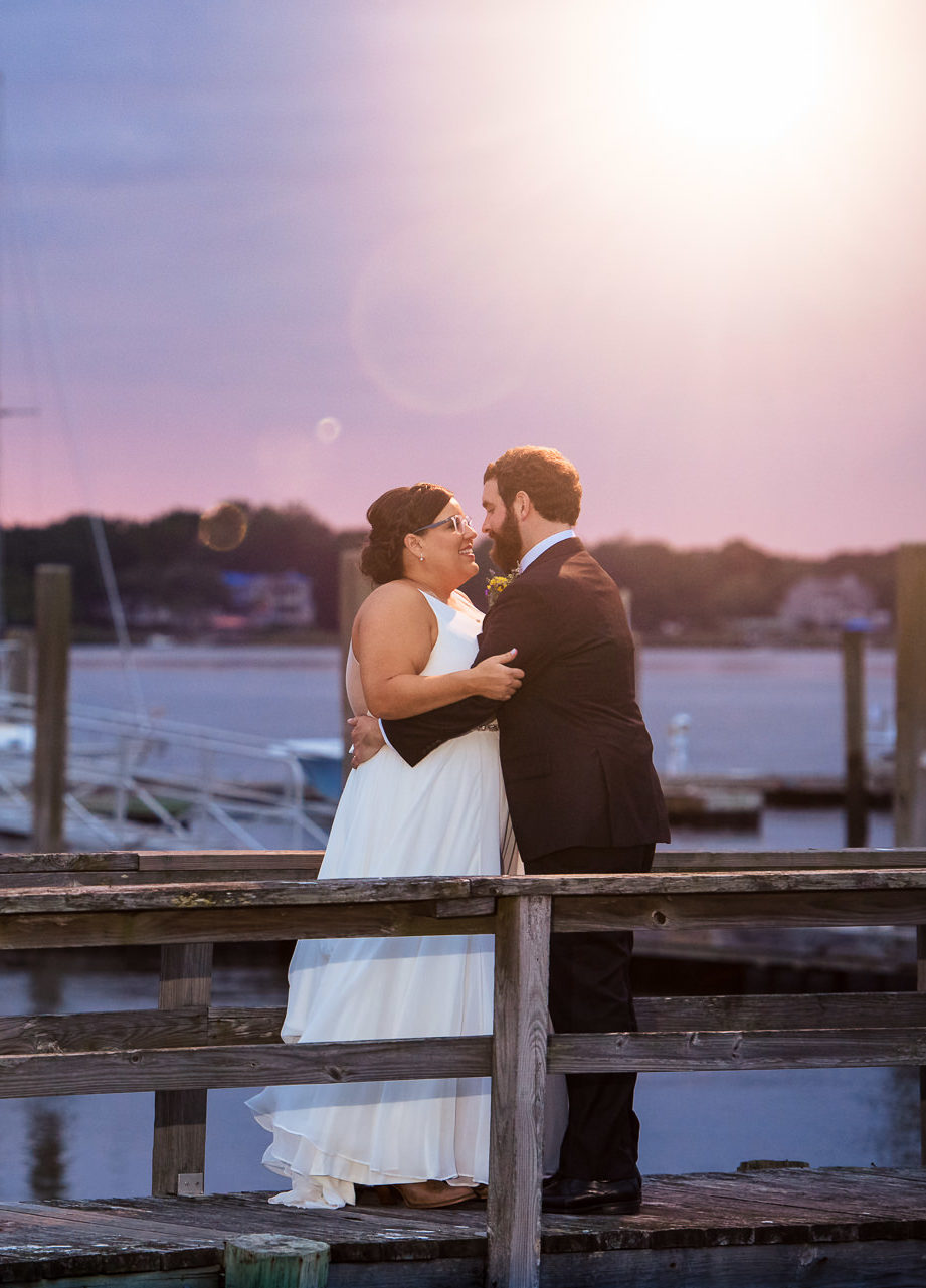 A bride and groom embracing on a dock, smiling, at sunset at The Island House in Charleston, SC by Charlotte wedding photographers DeLong Photography