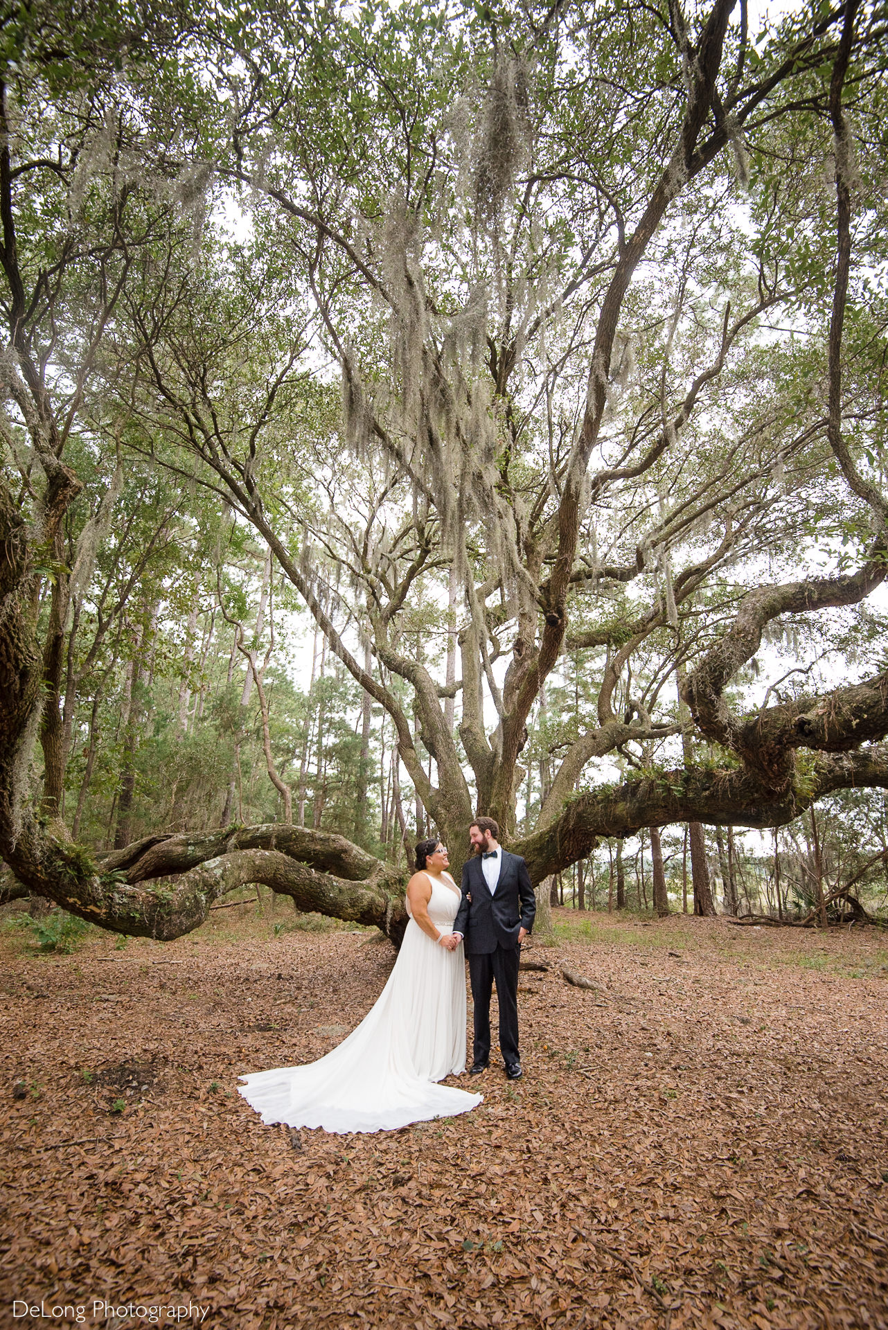 Bride and groom smiling at one another at the large oak tree on the property of the Island House in Charleston, SC by Charlotte Wedding Photographers DeLong Photography