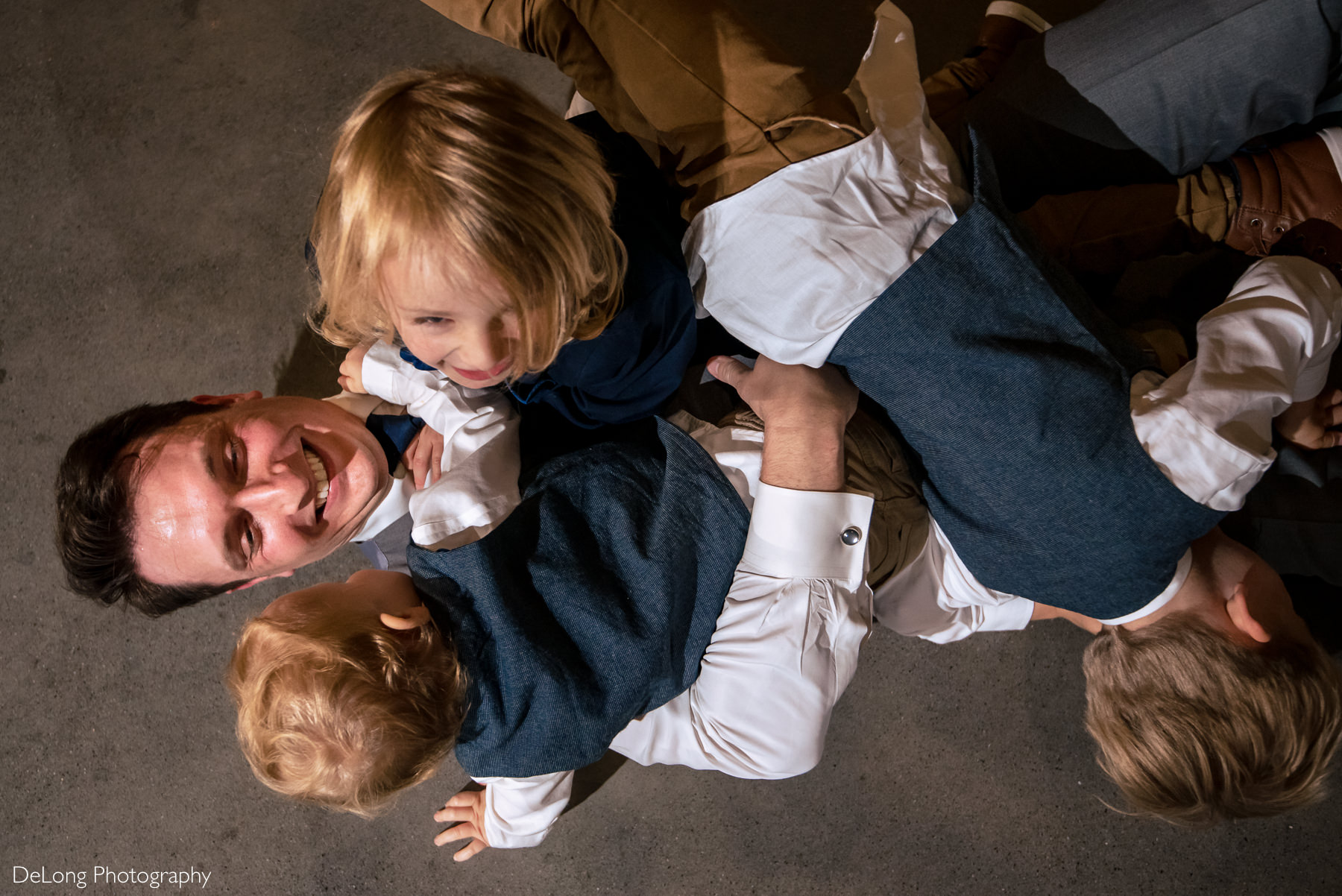 Man being dog-piled by children at Childress Vineyards by Charlotte Wedding Photographers DeLong Photography