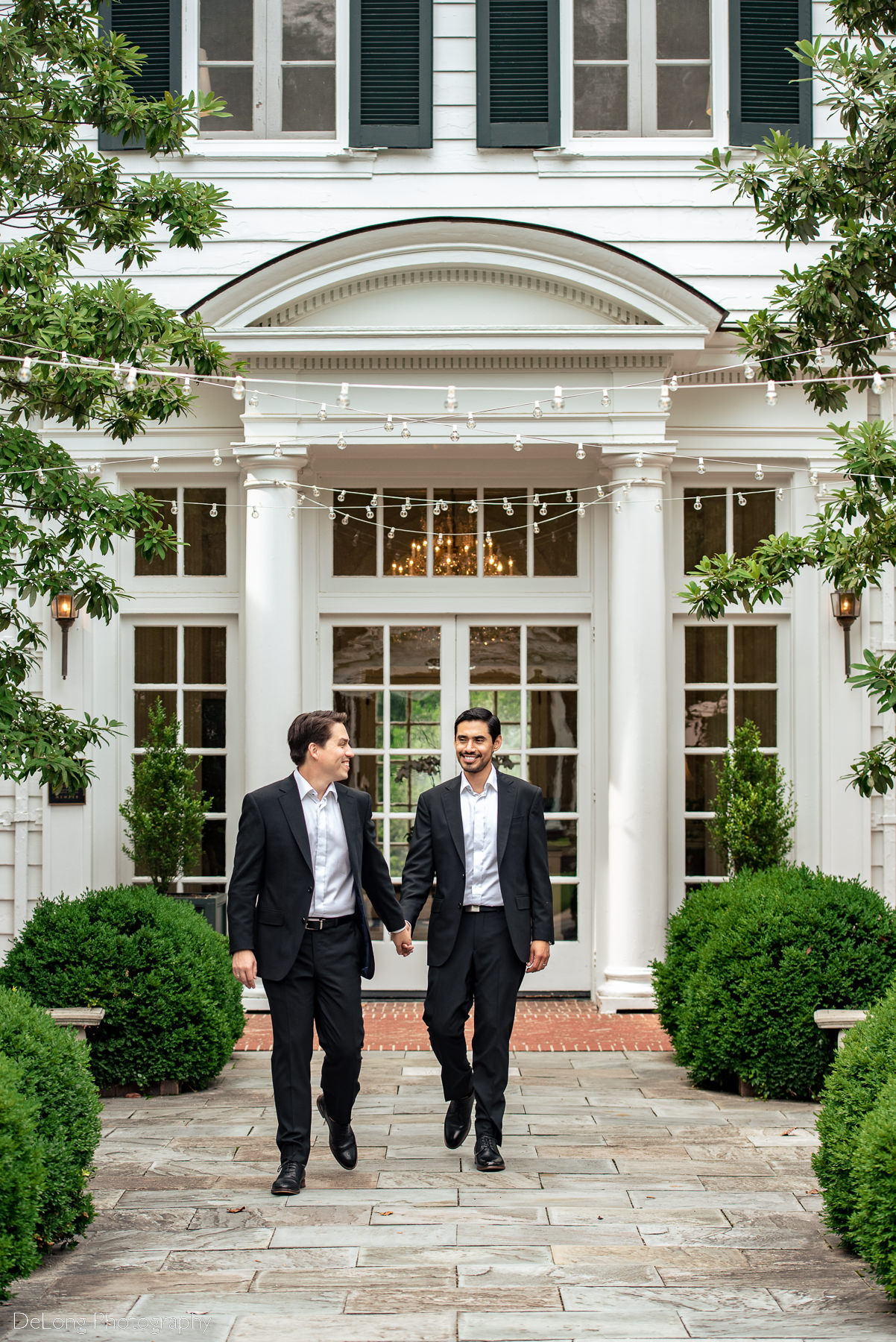Two grooms looking at each other and smiling outside the Duke Mansion  by Charlotte wedding photographers DeLong Photography