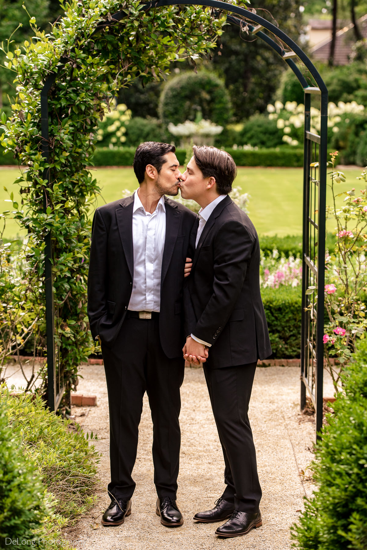Two grooms sharing a kiss under a garden arbor at the Duke Mansion by Charlotte wedding photographers DeLong Photography