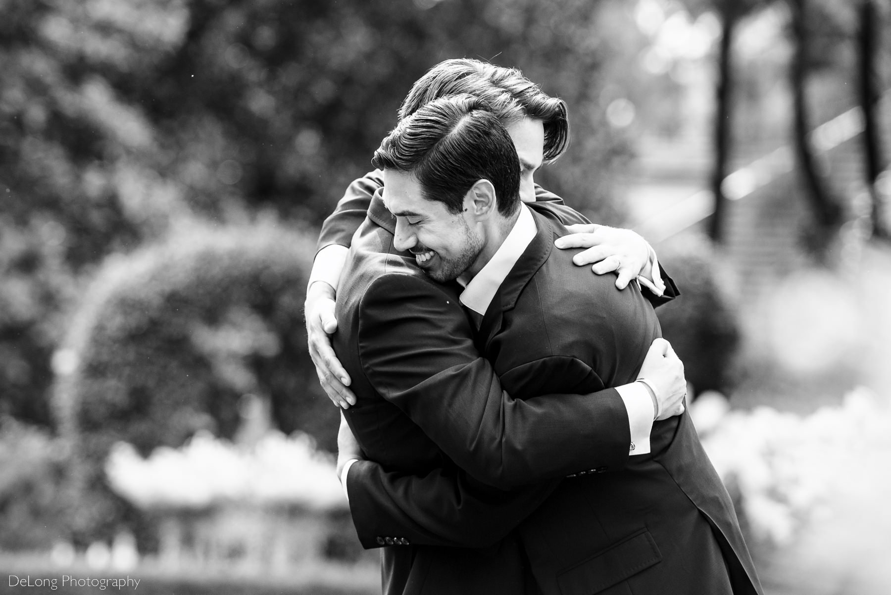 Black and white candid photograph of two grooms laughing and hugging at the Duke Mansion by Charlotte wedding photographers DeLong Photography