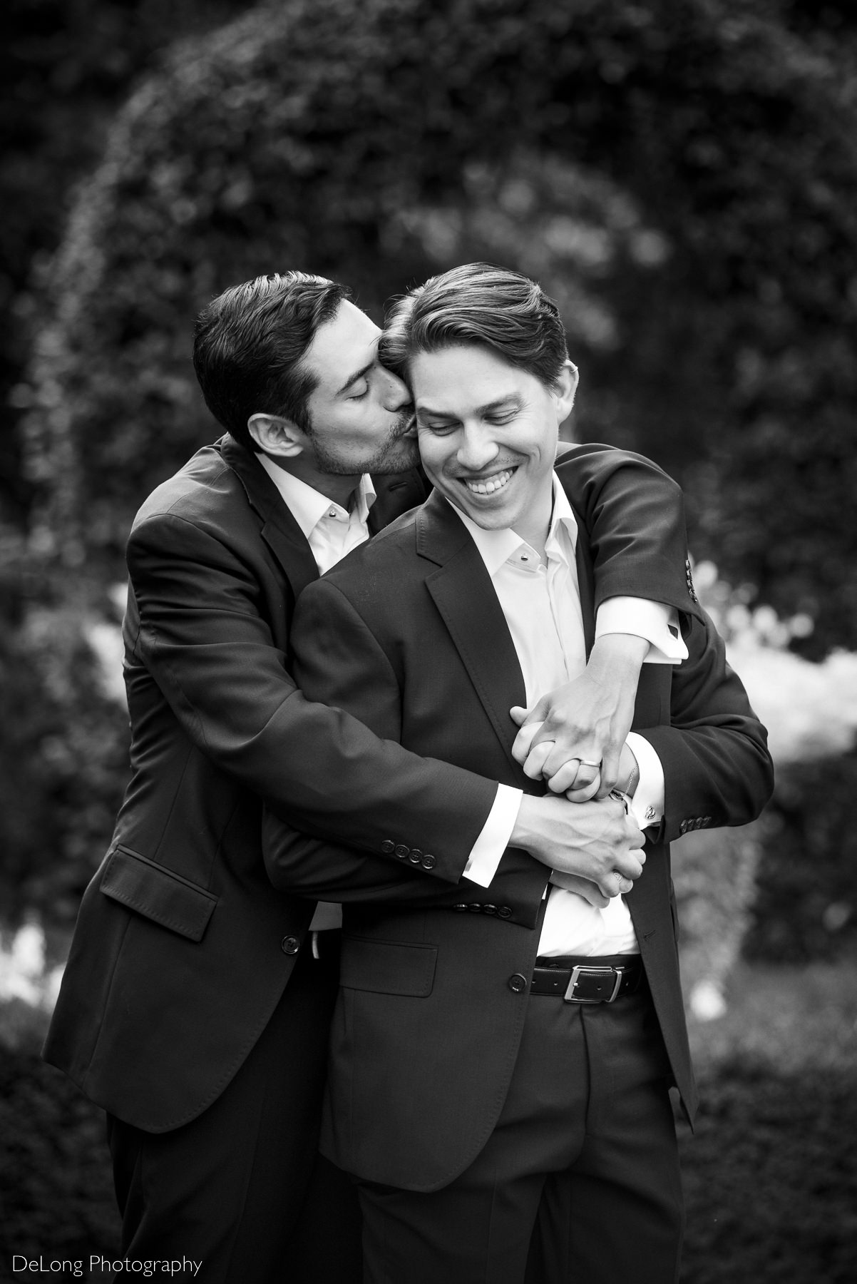 Black and white portrait of a groom giggling while getting a kiss on the cheek from his husband by Charlotte wedding photographers DeLong Photography