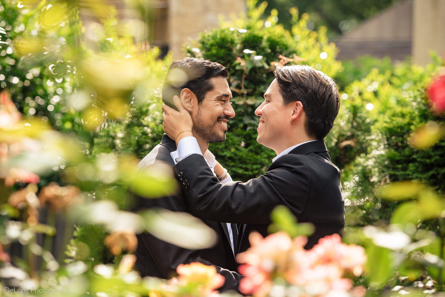 Portrait with bokeh leaves in the foreground of two grooms smiling at each other in the gardens of the Duke Mansion by Charlotte wedding photographers DeLong Photography