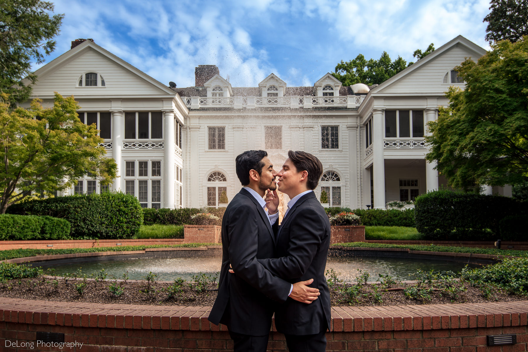 Portrait of two grooms just before their lips meet for a kiss in front of the Duke Mansion by Charlotte wedding photographers DeLong Photography