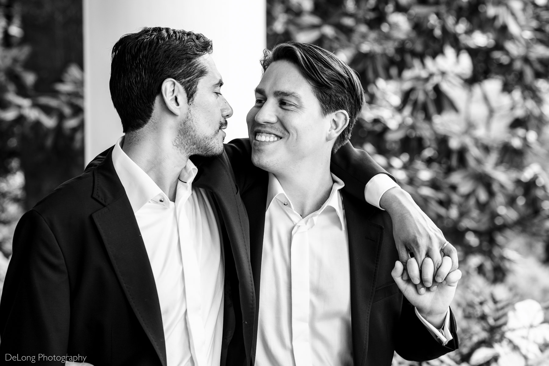 Black and white candid photograph of a groom smiling at his husband walking arm in arm in front of the Duke Mansion by Charlotte wedding photographers DeLong Photography