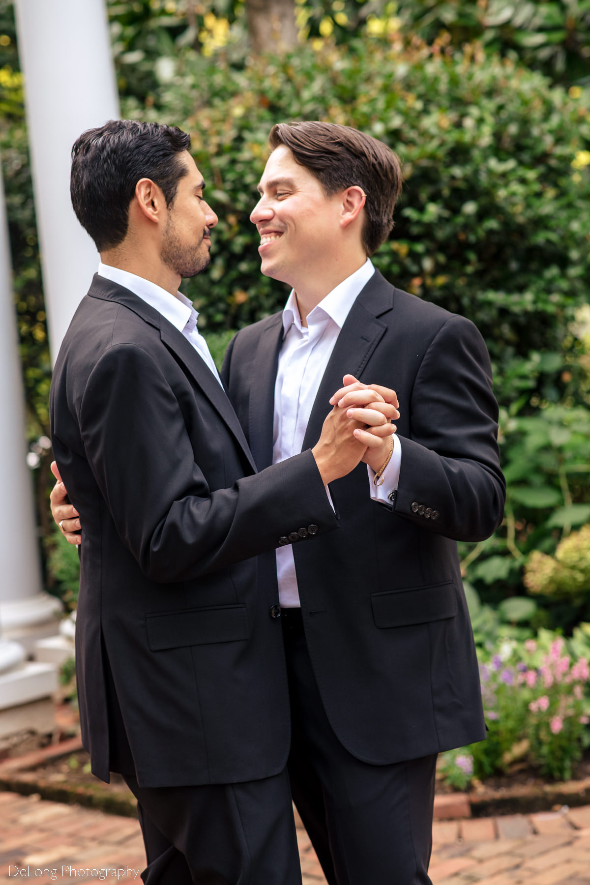 Candid moment of grooms laughing and smiling together dancing in the gardens of the Duke Mansion by Charlotte wedding photographers DeLong Photography