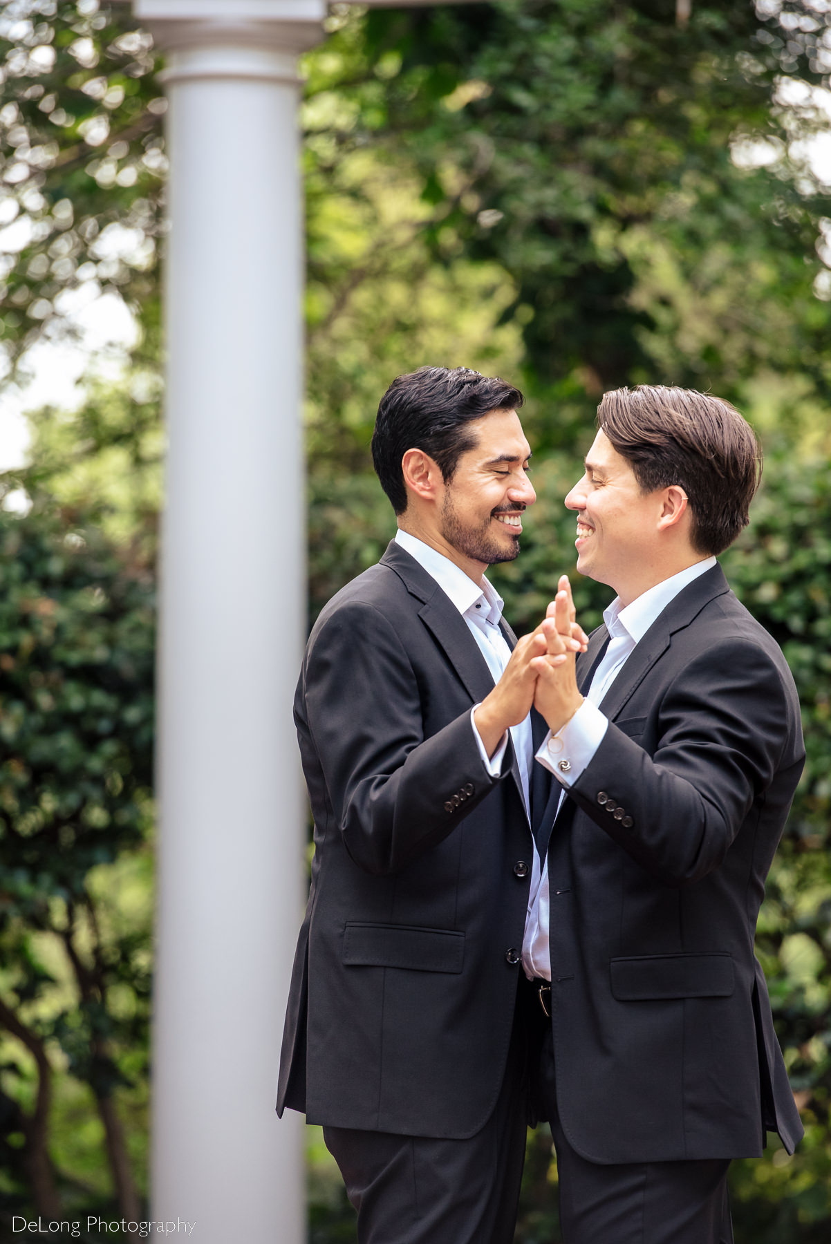 Candid moment of grooms laughing and smiling together dancing in the gardens of the Duke Mansion by Charlotte wedding photographers DeLong Photography