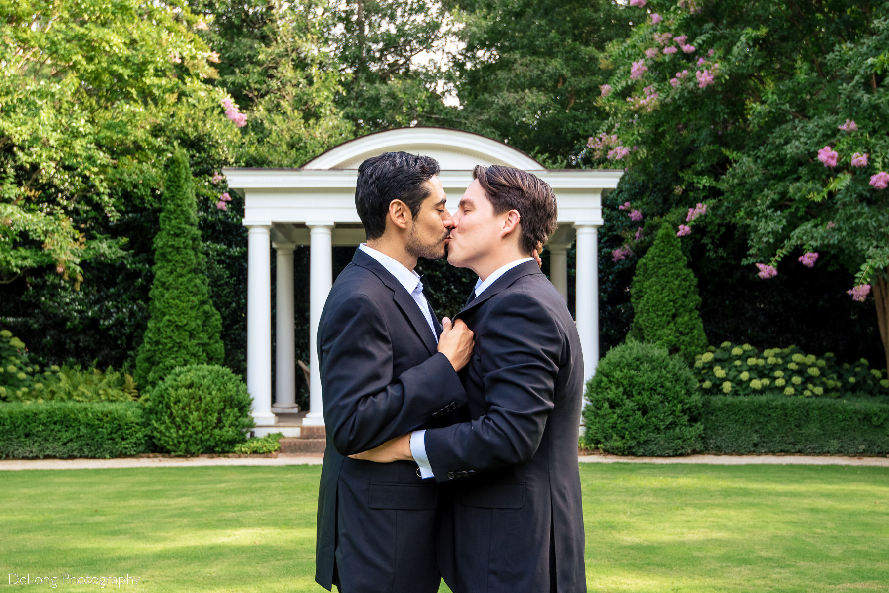 Grooms sharing a kiss in front of the columned patio of the Duke Mansion by Charlotte wedding photographers DeLong Photography