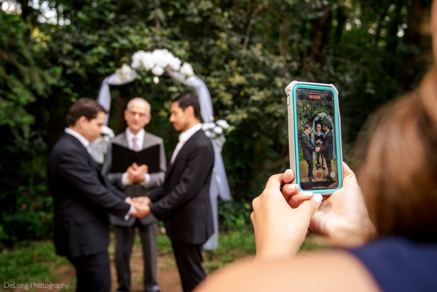Photo of a cell phone screen that is focused on the same-sex elopement taking place which can also be seen blurry in the background by Charlotte wedding photographers DeLong Photography