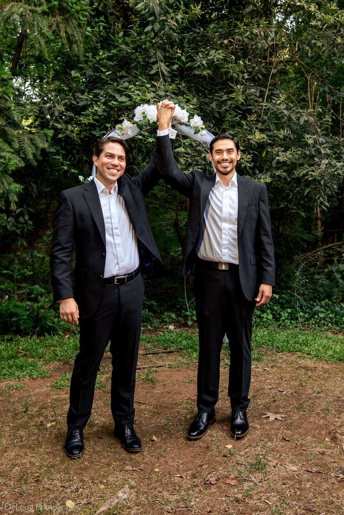 Two grooms raising hands together in joy after their same-sex elopement by Charlotte wedding photographers DeLong Photography
