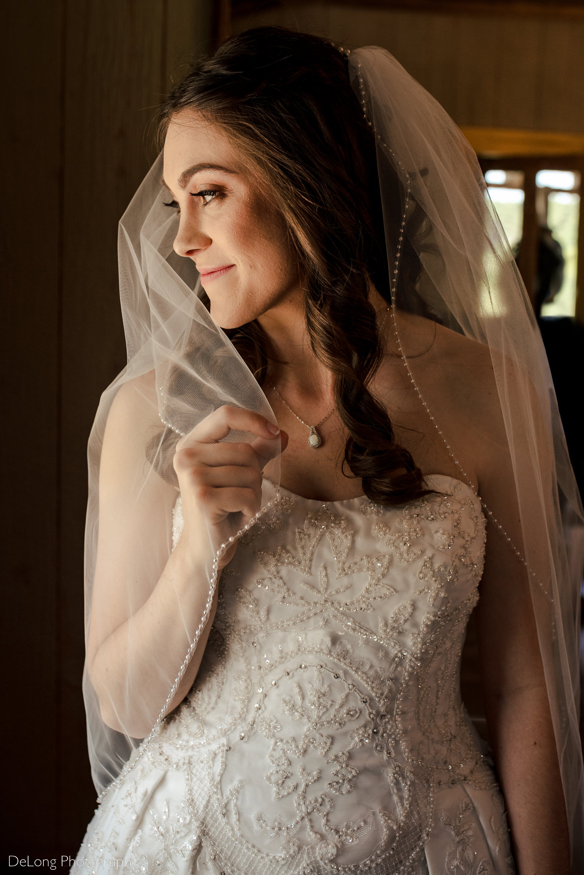 Bride touching her veil, smiling looking out the window of the bridal suite at Lady Bird Farms by Charlotte Wedding Photographers DeLong Photography