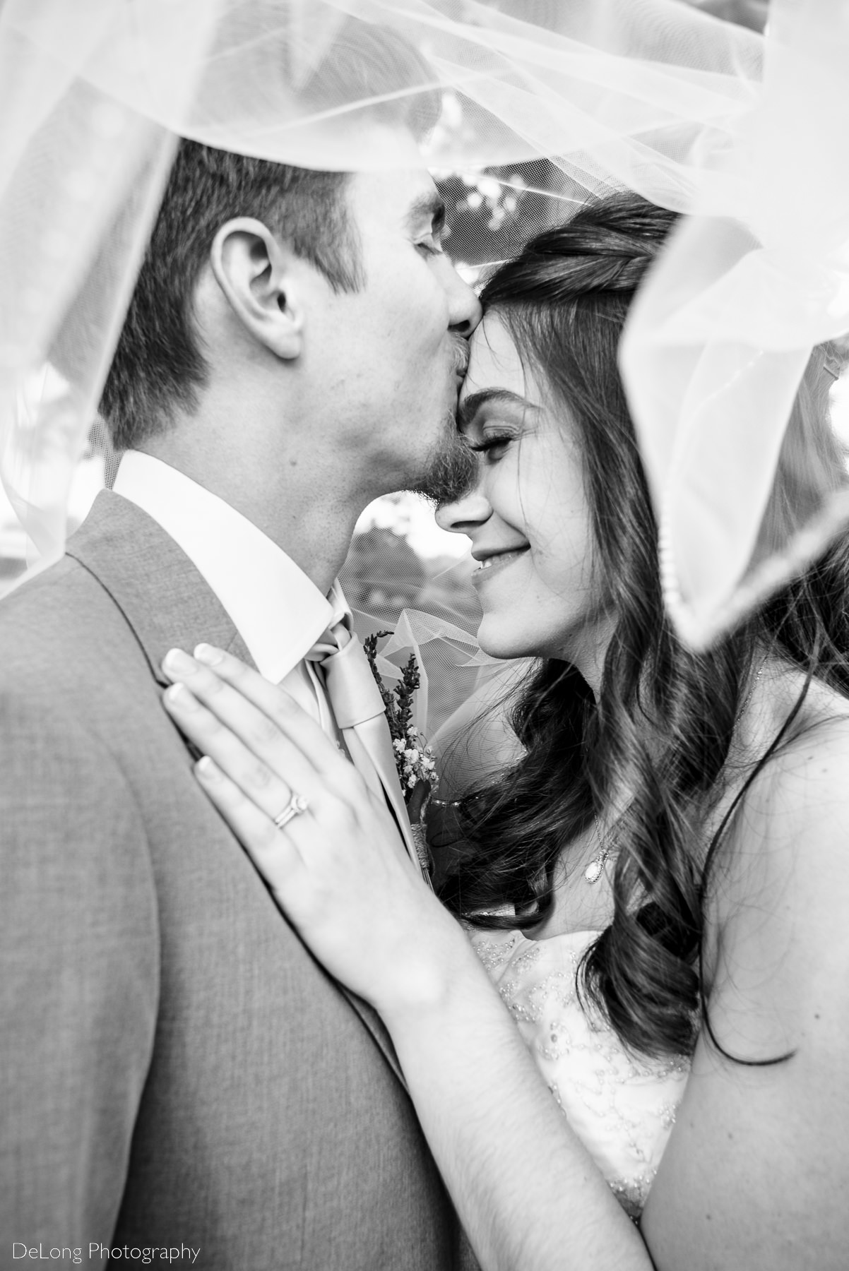 Bride and groom giggling while he kisses her forehead, under her veil by Charlotte Wedding Photographers DeLong Photography