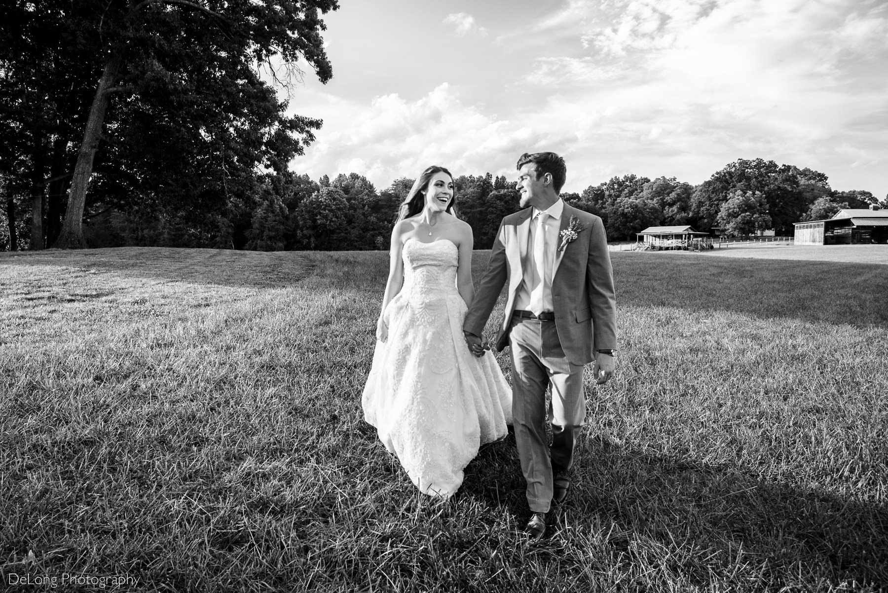 Black and white image of bride and groom walking in an open field smiling at one another at Lady Bird Farms by Charlotte Wedding Photographers DeLong Photography